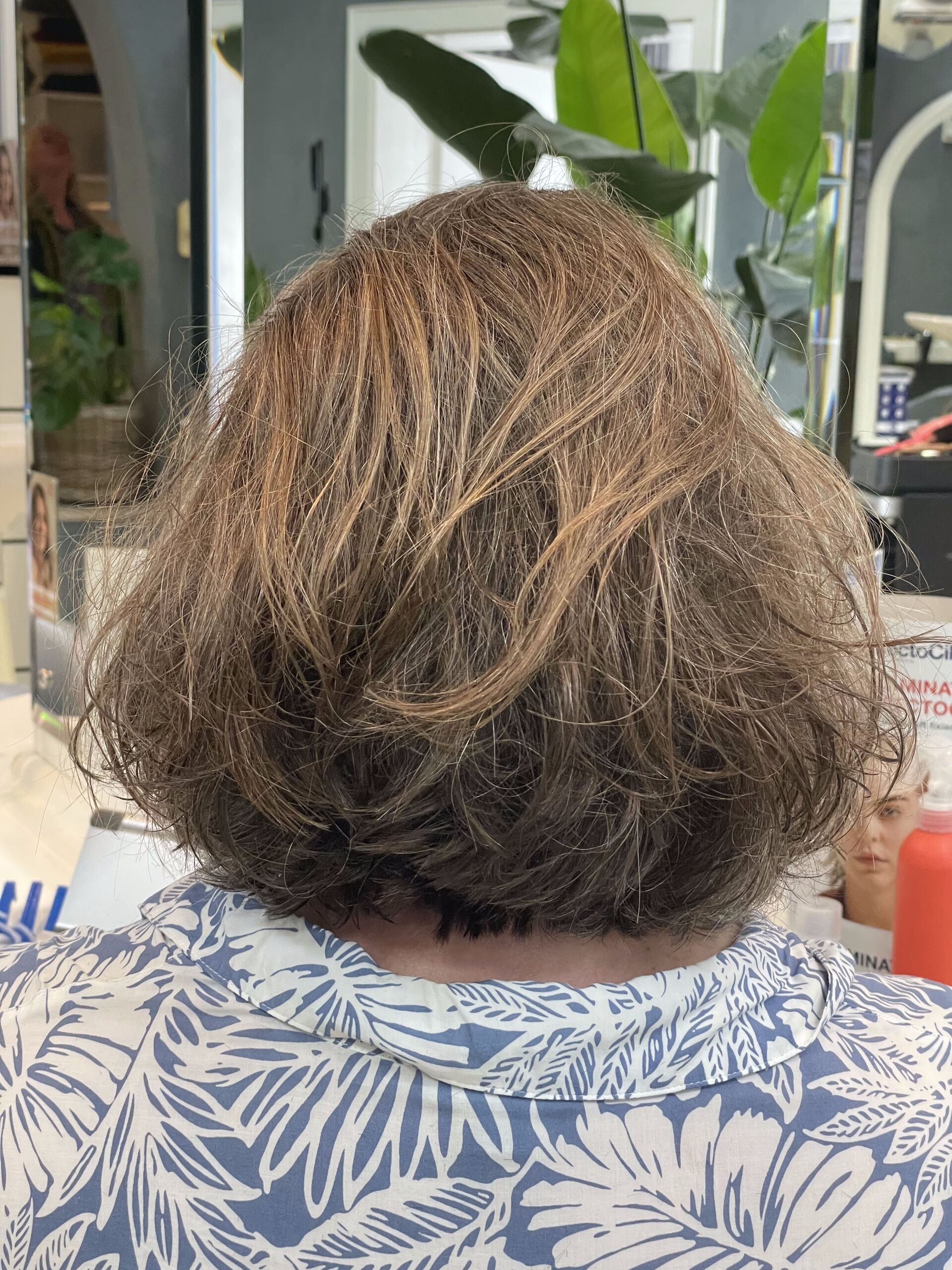 Rücken einer Person mit kurzen, braunen Haaren und einem blau-weißen Blumenhemd in einem Salon.