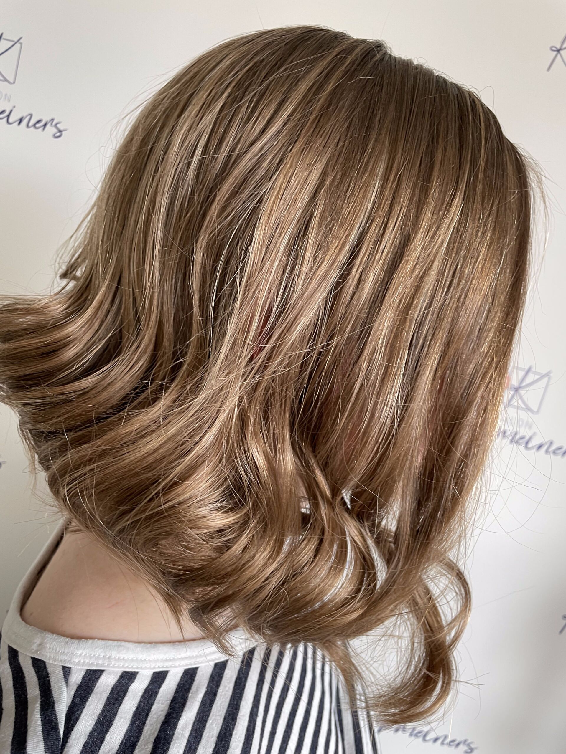 Frau mit schulterlangem braunem Haar, leicht gewellt, in gestreiftem Hemd, Profilansicht.