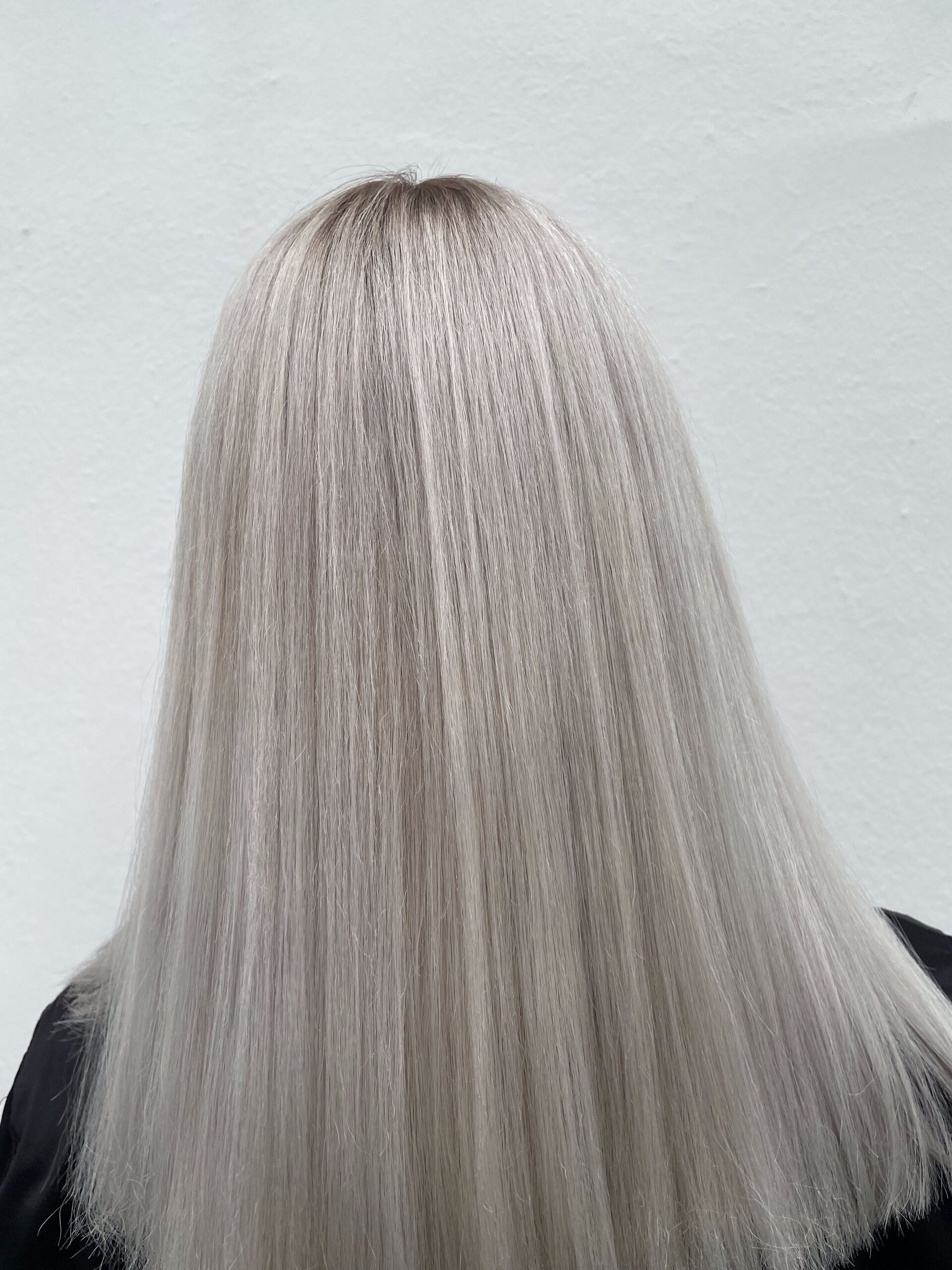 Frauenhaar, gekräuselt und platinblond gefärbt mit dunklen Ansätzen, vor weißem Hintergrund.