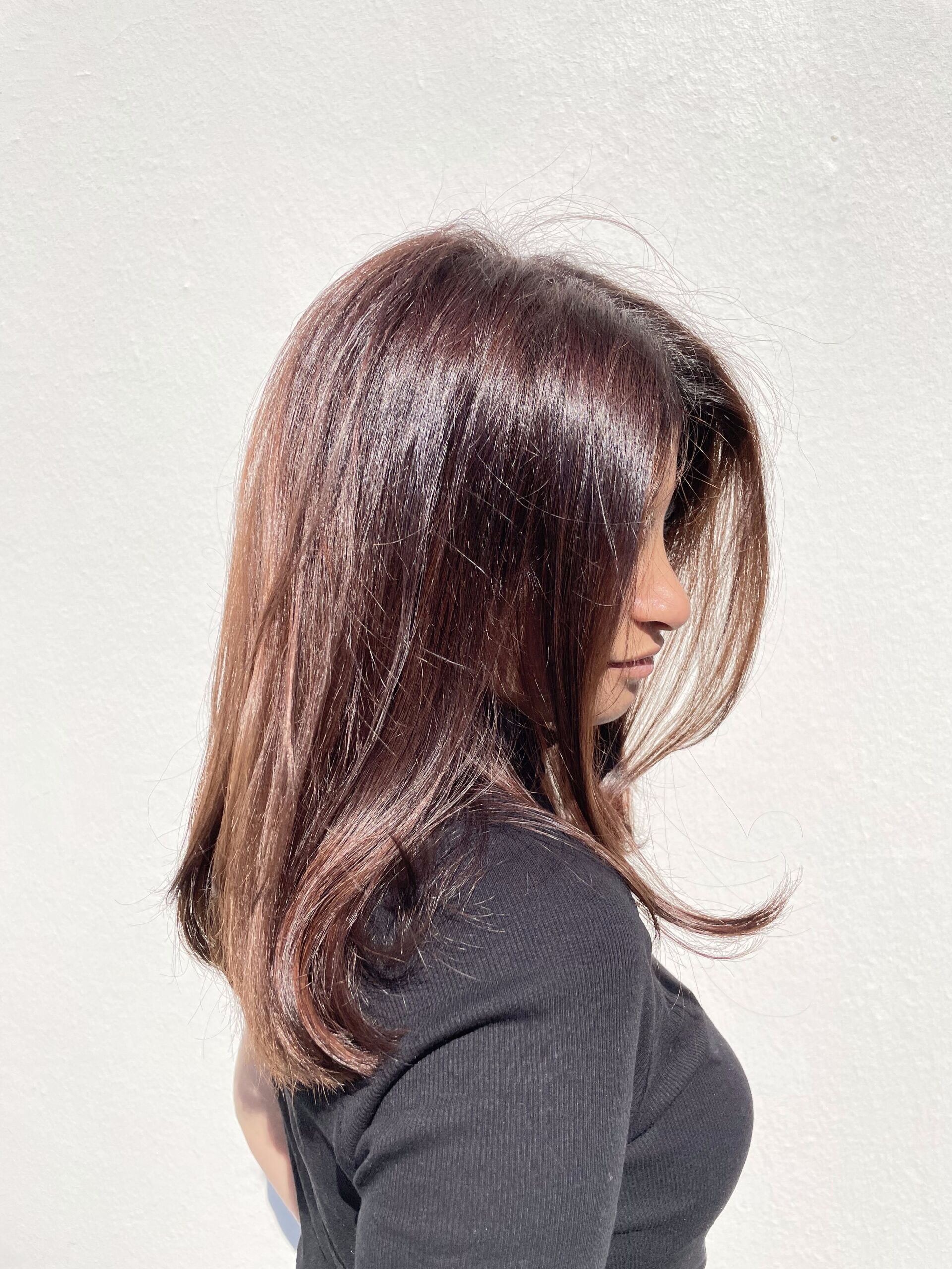 Frau mit langem, rotbraunem Haar, leicht von der Kamera abgewandt, mit dunklem Oberteil bekleidet, in heller Umgebung.