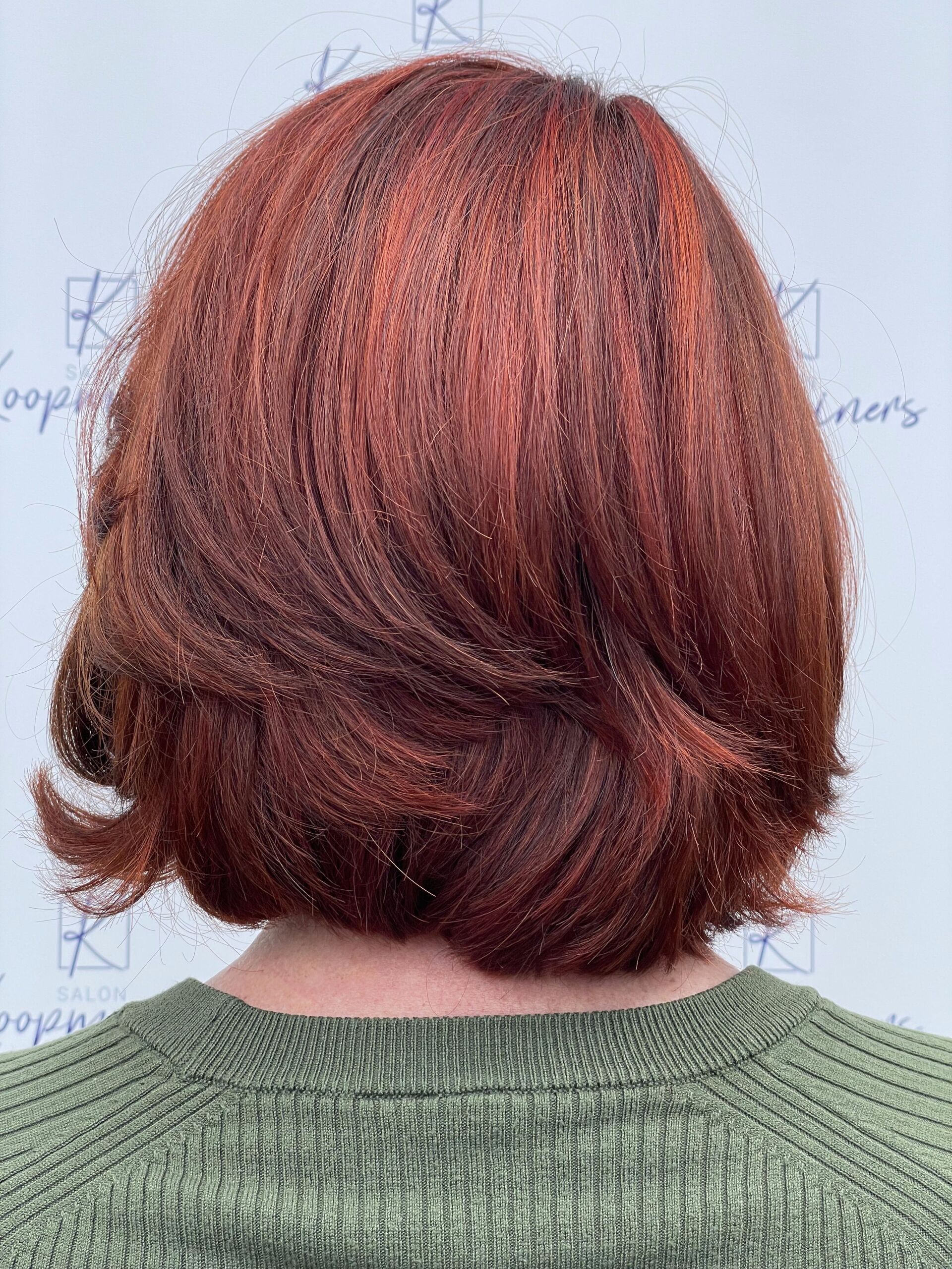 Frau mit gestuftem, rotbraunem Bob-Haarschnitt, trägt einen grünen Pullover.