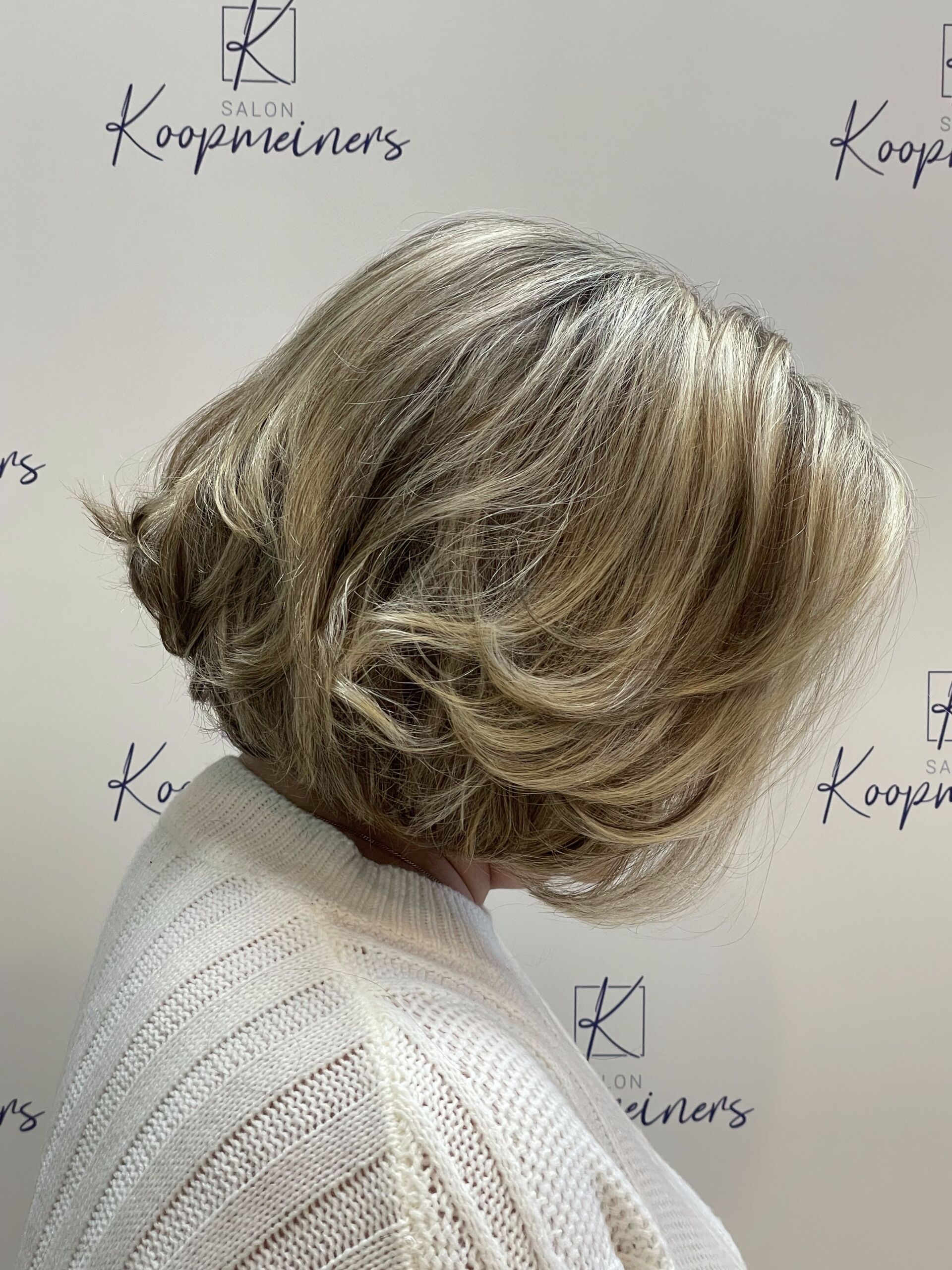 Frau mit gestuftem, hellbraunem Haar, trägt einen weißen Strickpullover