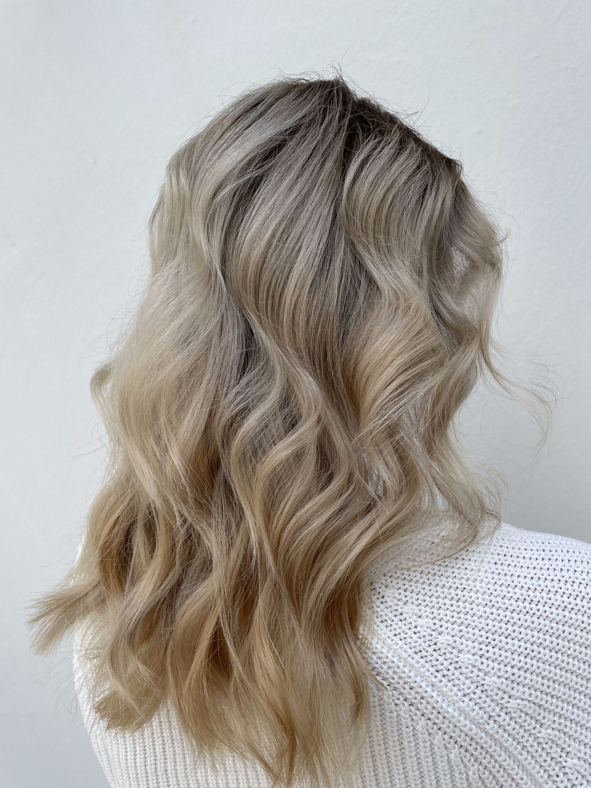 Frau mit welligem, hellblondem Haar, trägt einen weißen Pullover vor weißem Hintergrund.