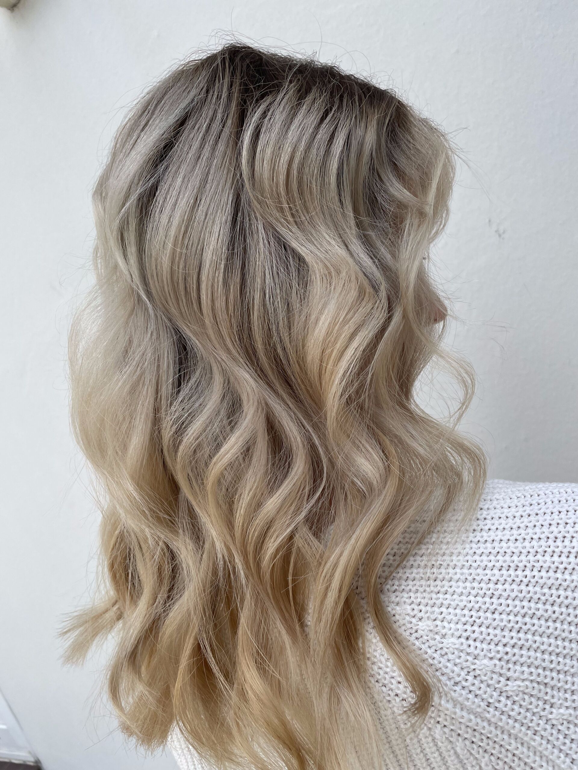 Frau mit welligem blondem Haar, dunklen Haarwurzeln und hellem Hintergrund.