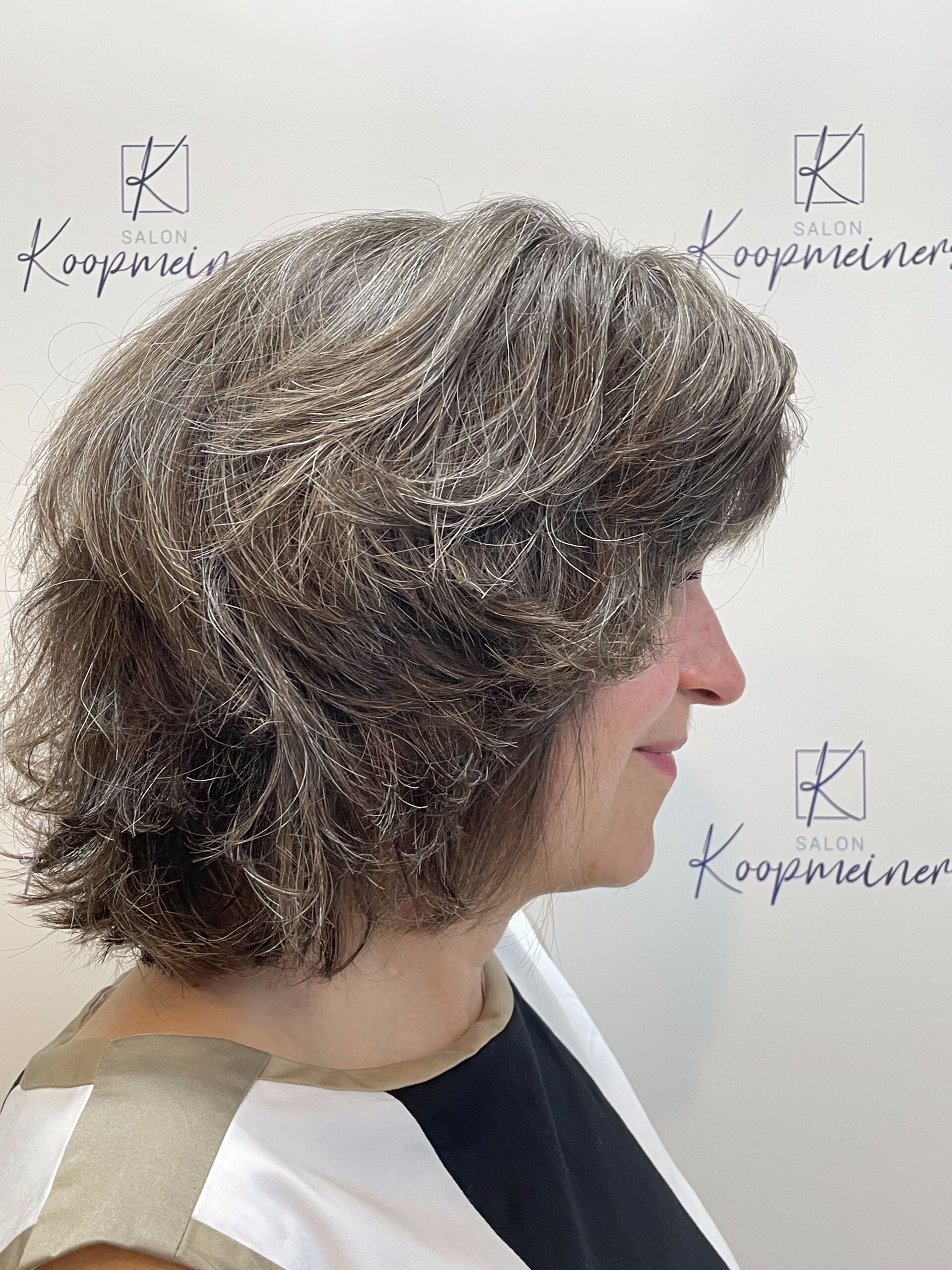 Frau mit gestuftem, grauem Haar, im Profil, lächelt leicht. Sie trägt ein schwarz-weißes Oberteil.