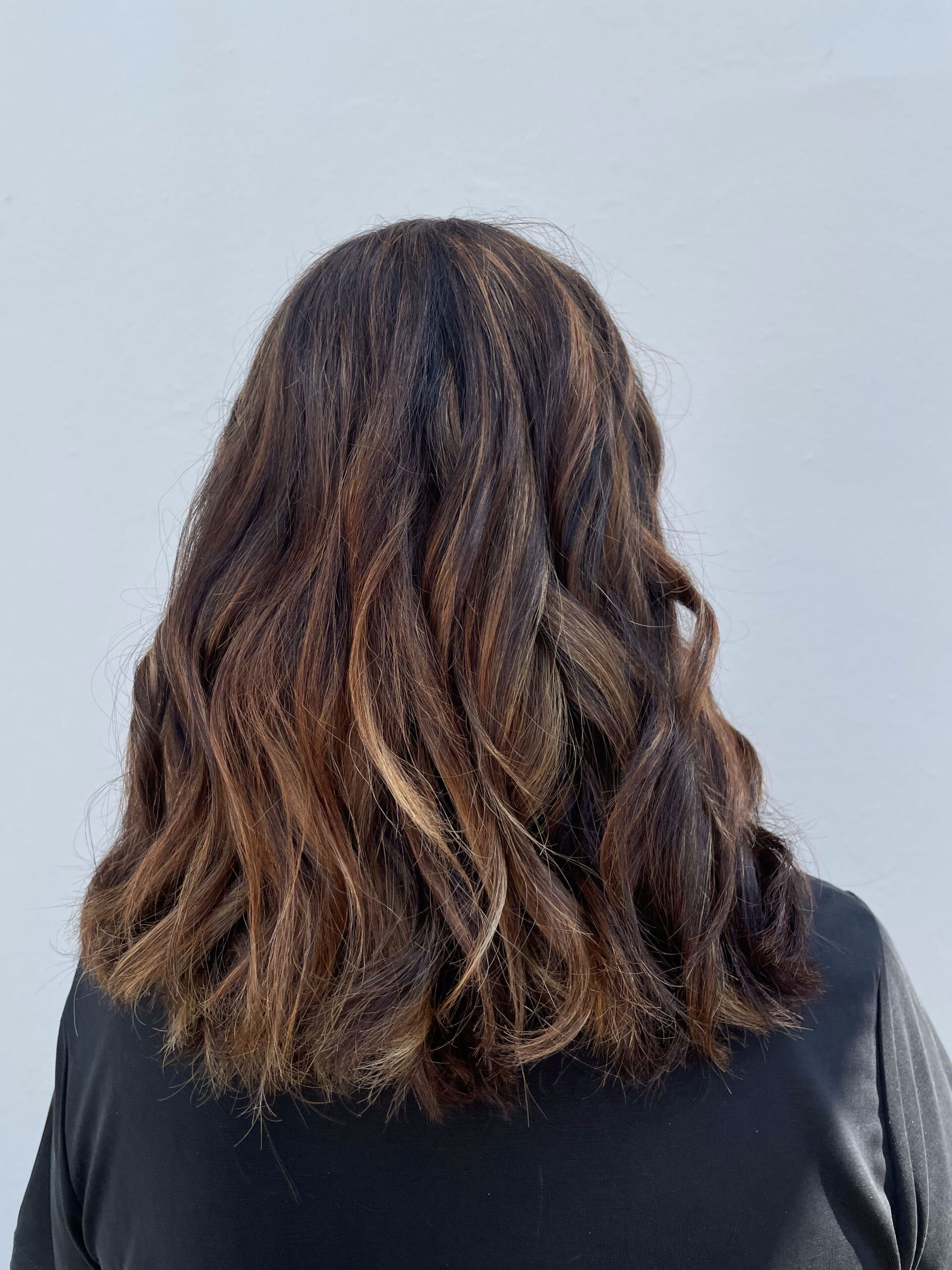 Frau mit welligem braunem Haar mit blonden Strähnchen, trägt ein schwarzes Oberteil vor weißem Hintergrund.