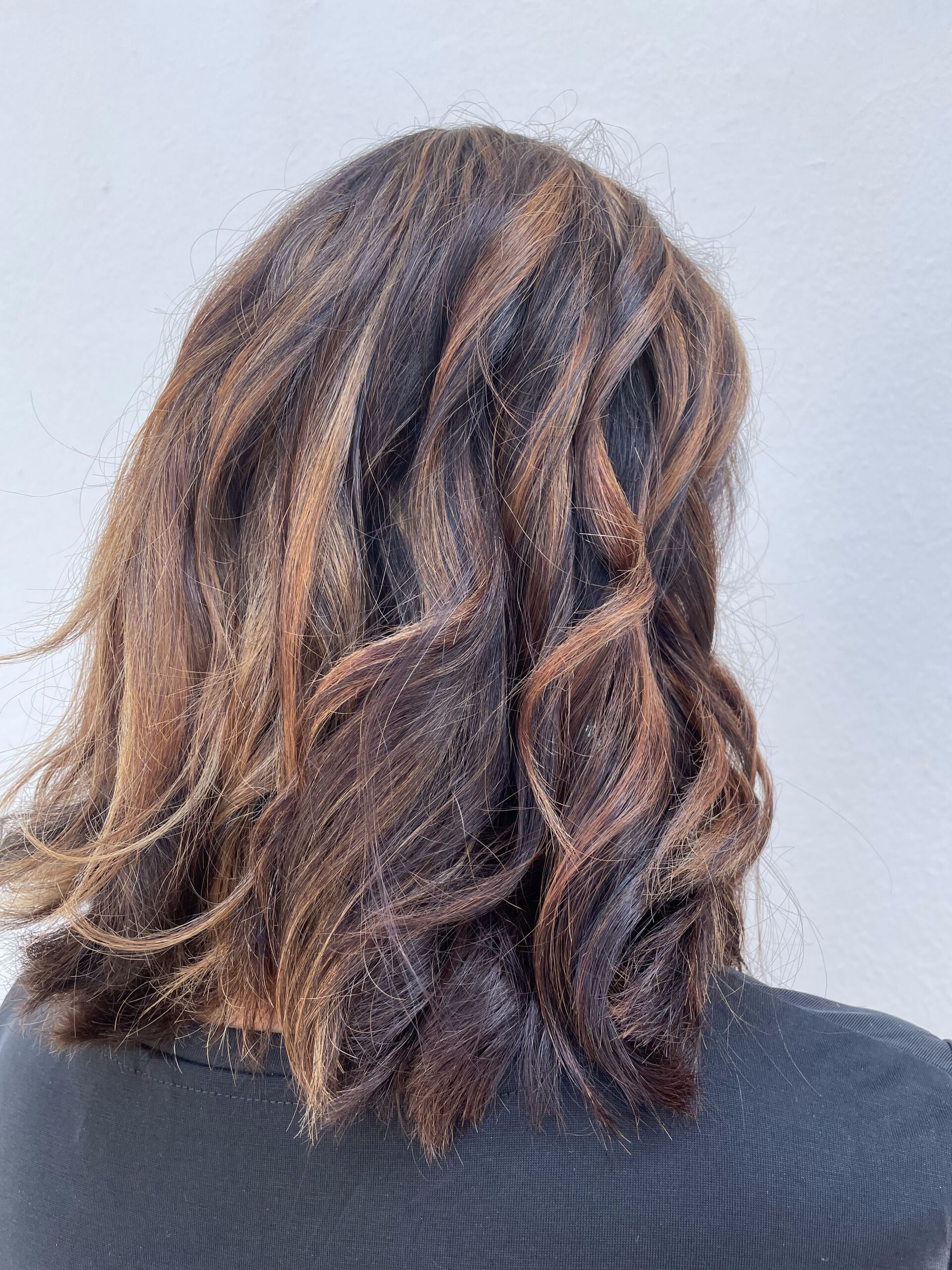 Frau mit dunklem, welligem Haar mit braunen Strähnchen, von hinten gesehen.