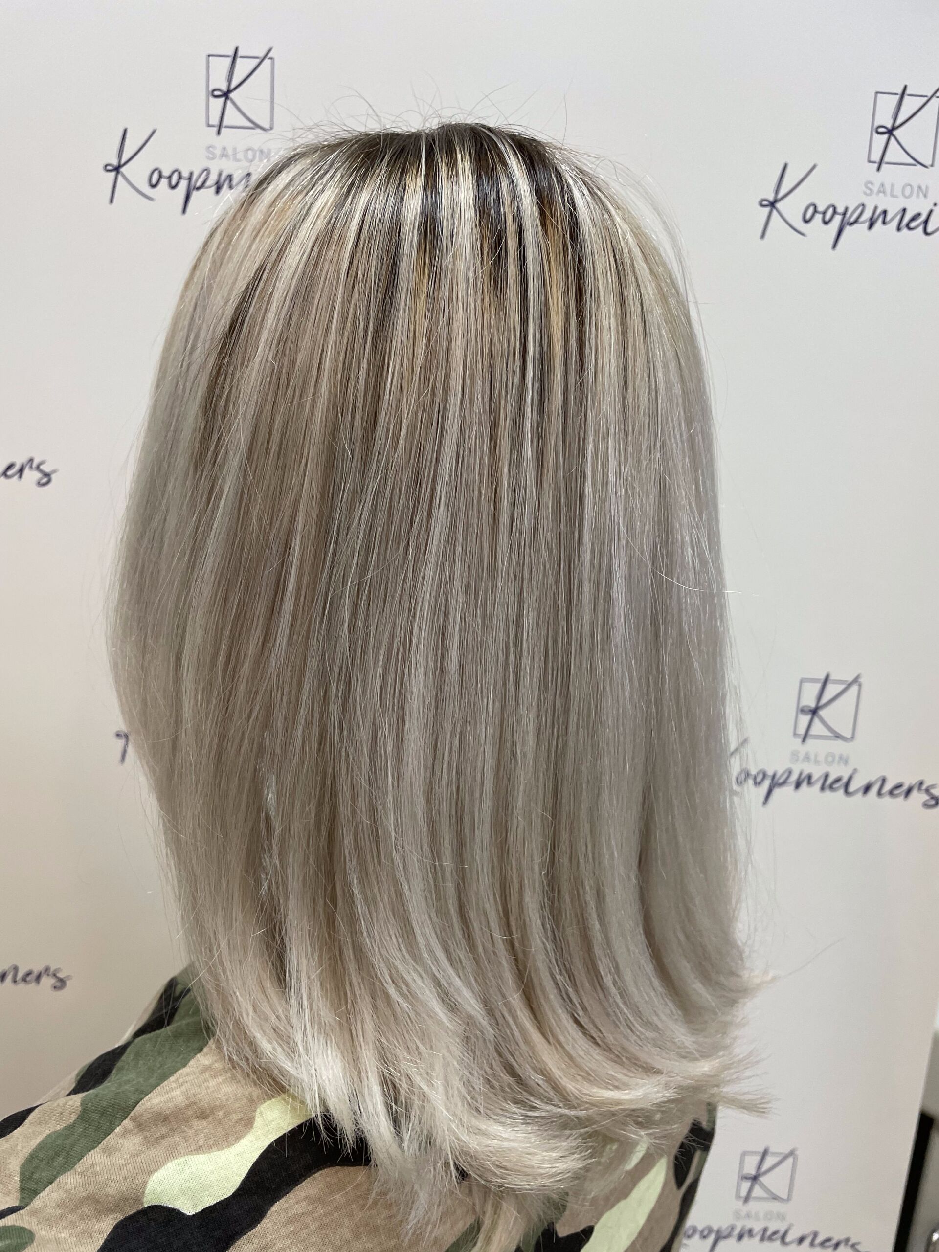 Frau mit platinblondem Bob-Haarschnitt, dessen Haaransatz sichtbar ist. Sie trägt ein Oberteil mit Camouflage-Muster.