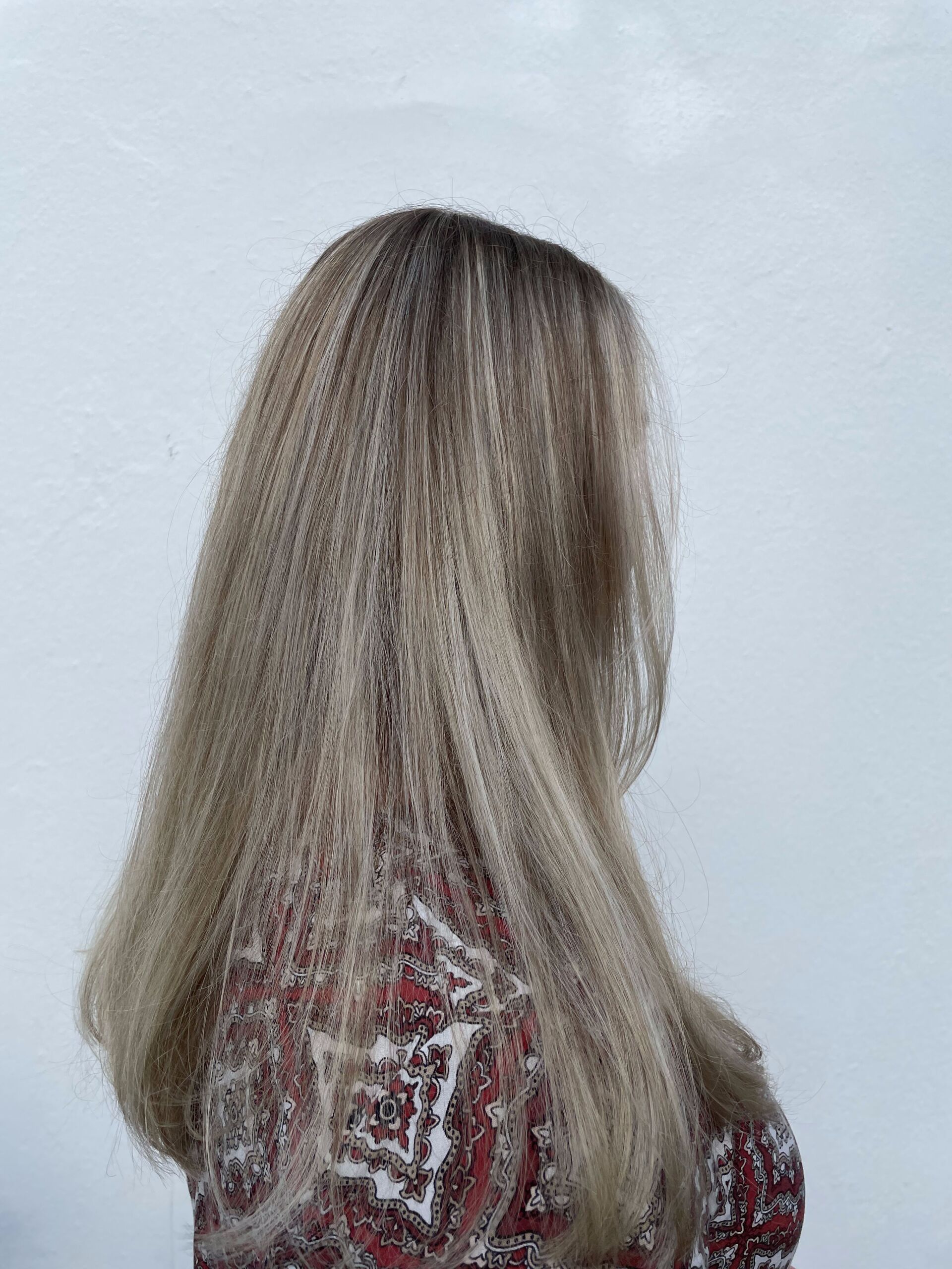 Frau mit langen, blonden Haaren, zur Seite gewandt, trägt ein gemustertes rotes Hemd vor weißem Hintergrund.