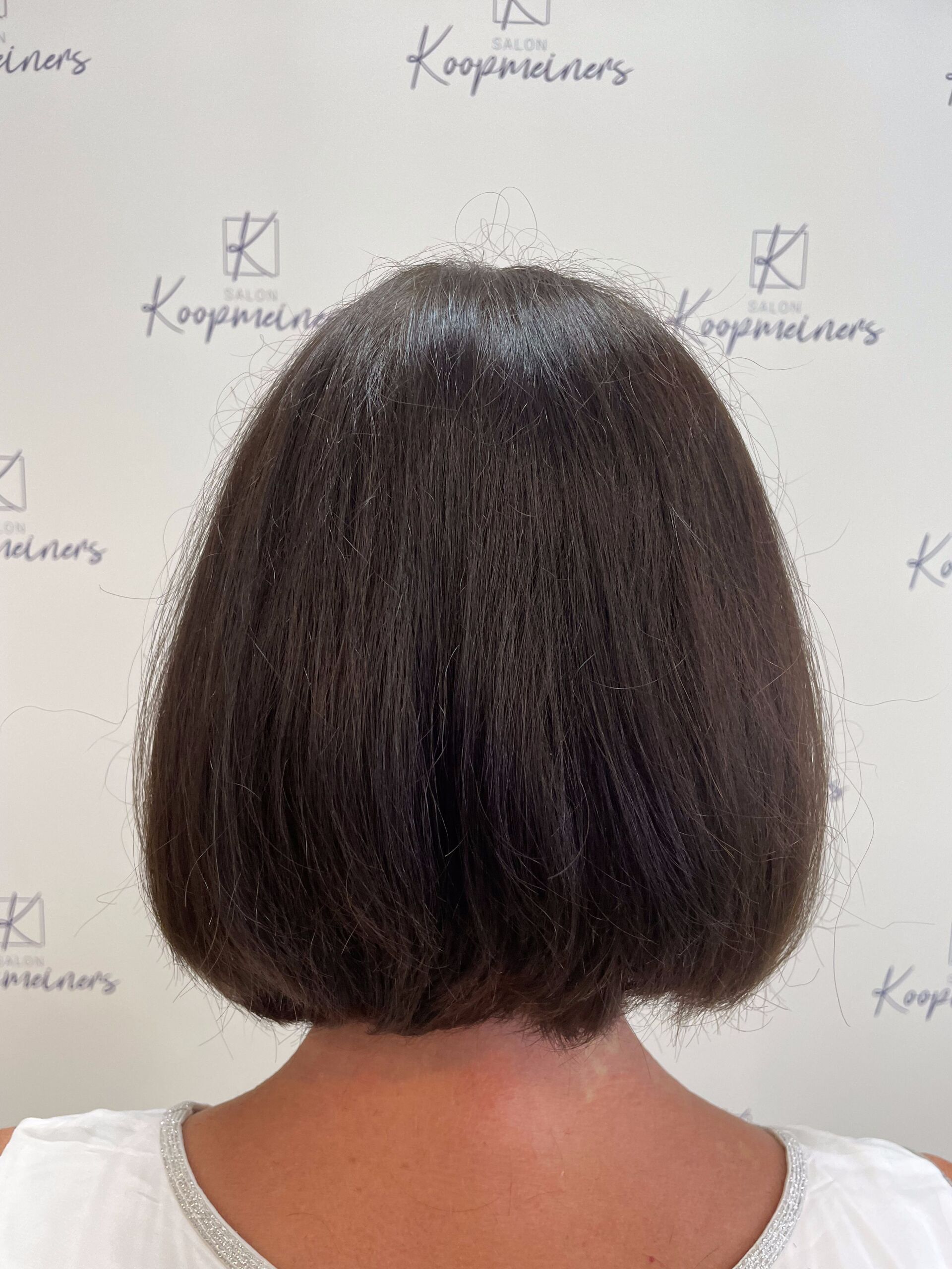 Rückansicht einer Person mit kurzem, dunklem, glattem Bob-Haarschnitt. Weißer Hintergrund mit Text.