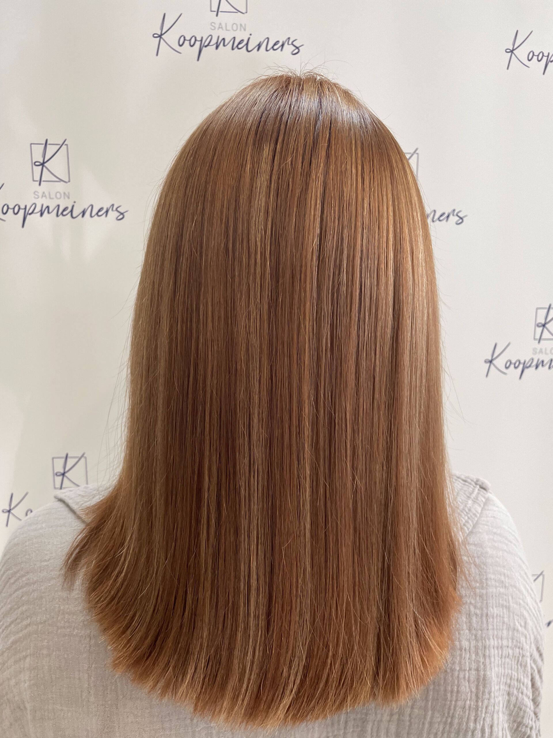 Frau mit langem, gekräuseltem, rotbraunem Haar, stumpf geschnitten an den Schultern, vor weißem Hintergrund.