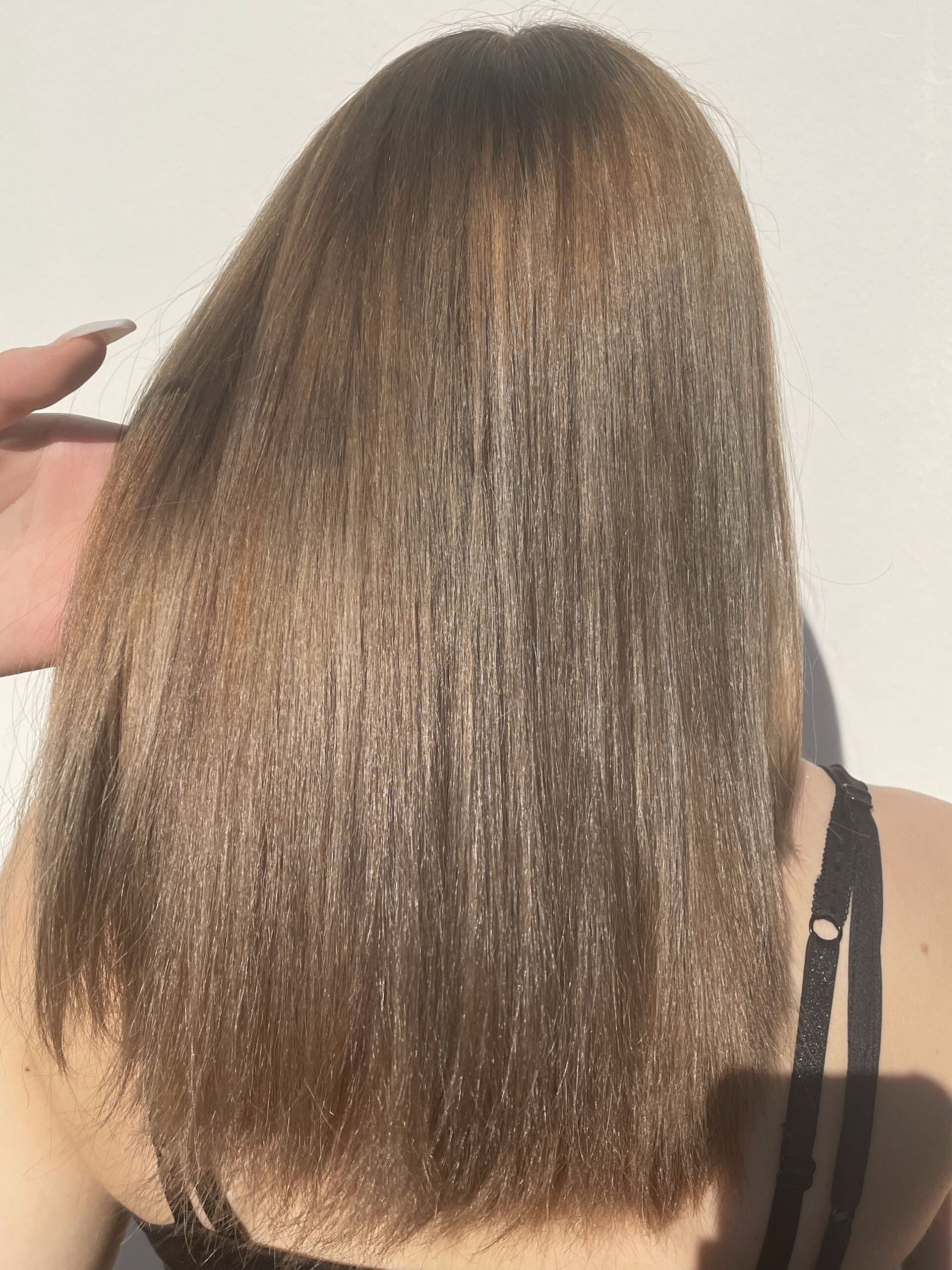 Glattes, braunes Haar einer Frau mit hellen Strähnchen wird vor einem weißen Hintergrund von einer Hand berührt.