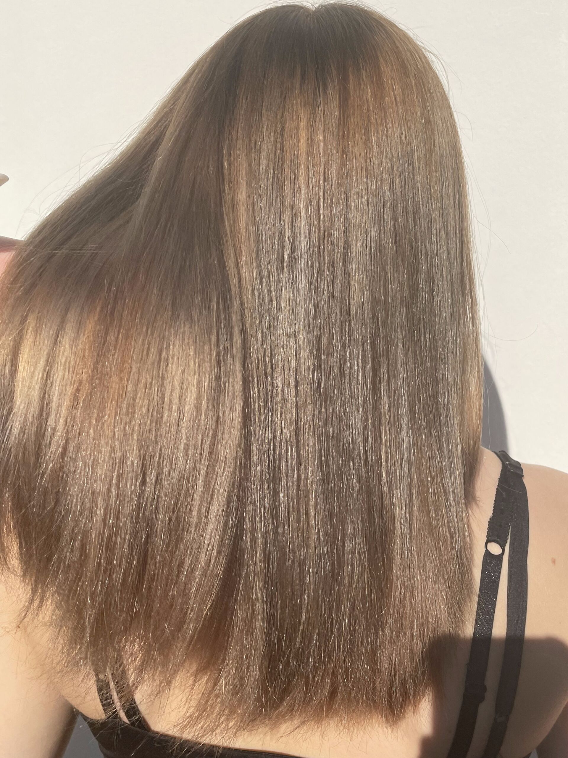 Frau mit glattem, hellbraunem Haar, mit dem Rücken zur Kamera gerichtet, im Sonnenlicht.