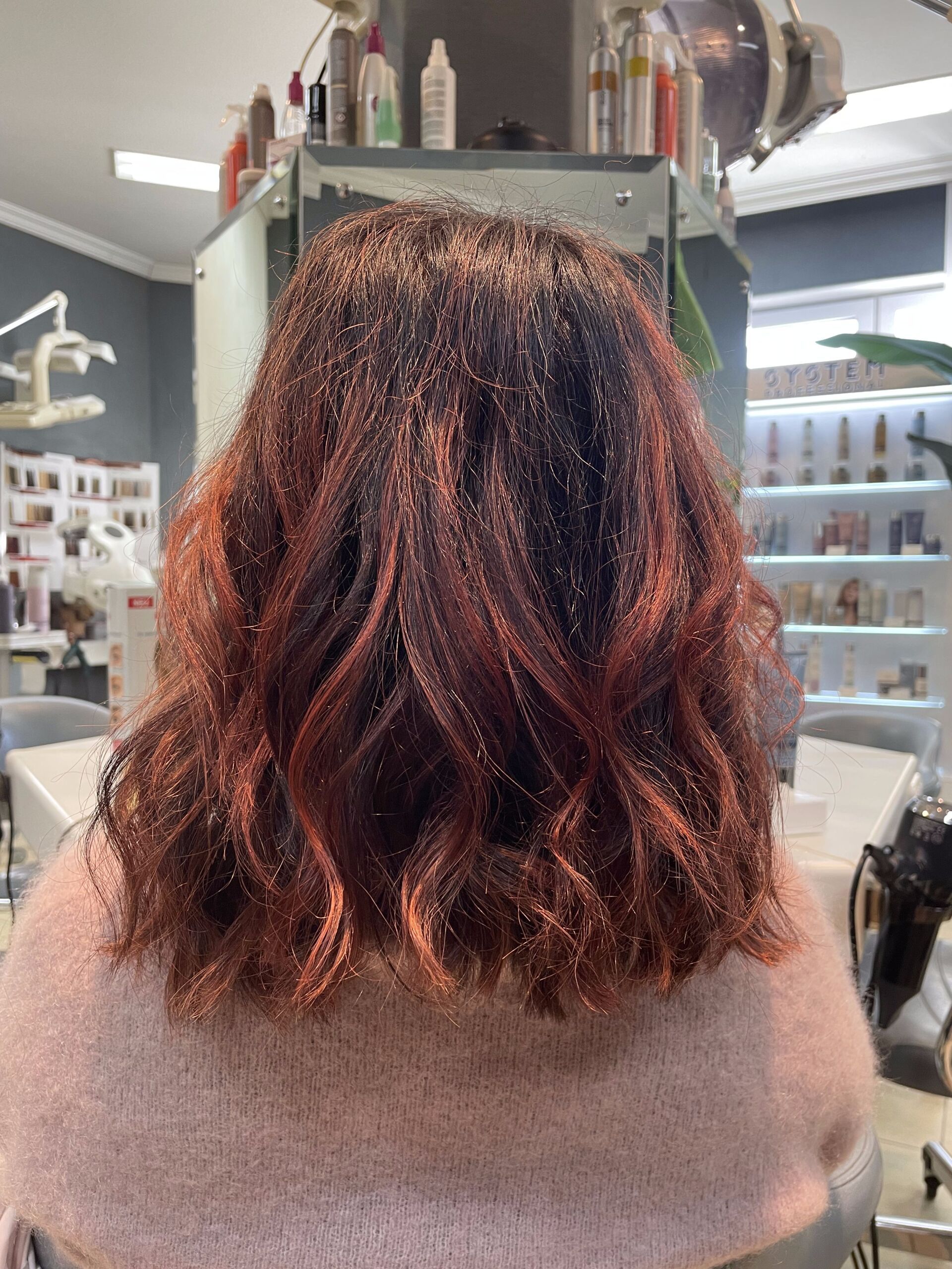 Frau mit welligem, rotbraunem Haar in einem Salon.