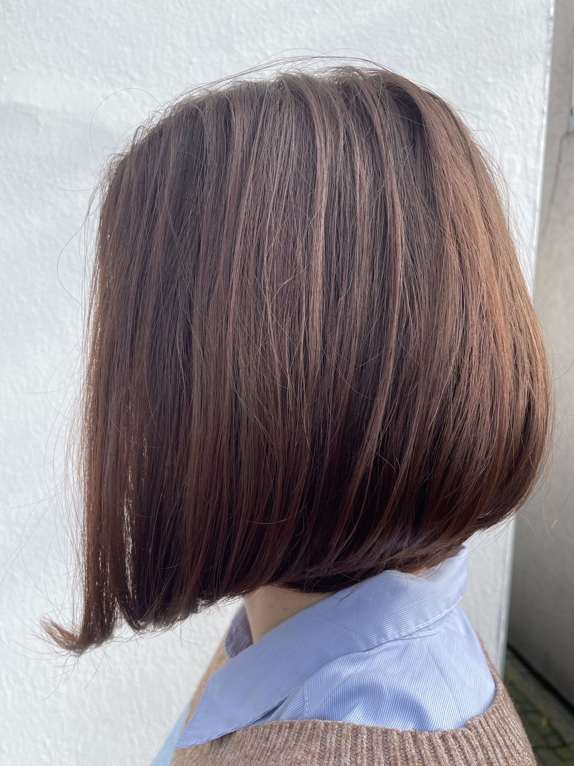 Frau mit kurzer, brauner, gestufter Bob-Frisur, trägt ein blaues Hemd mit Kragen und einen beigen Pullover.