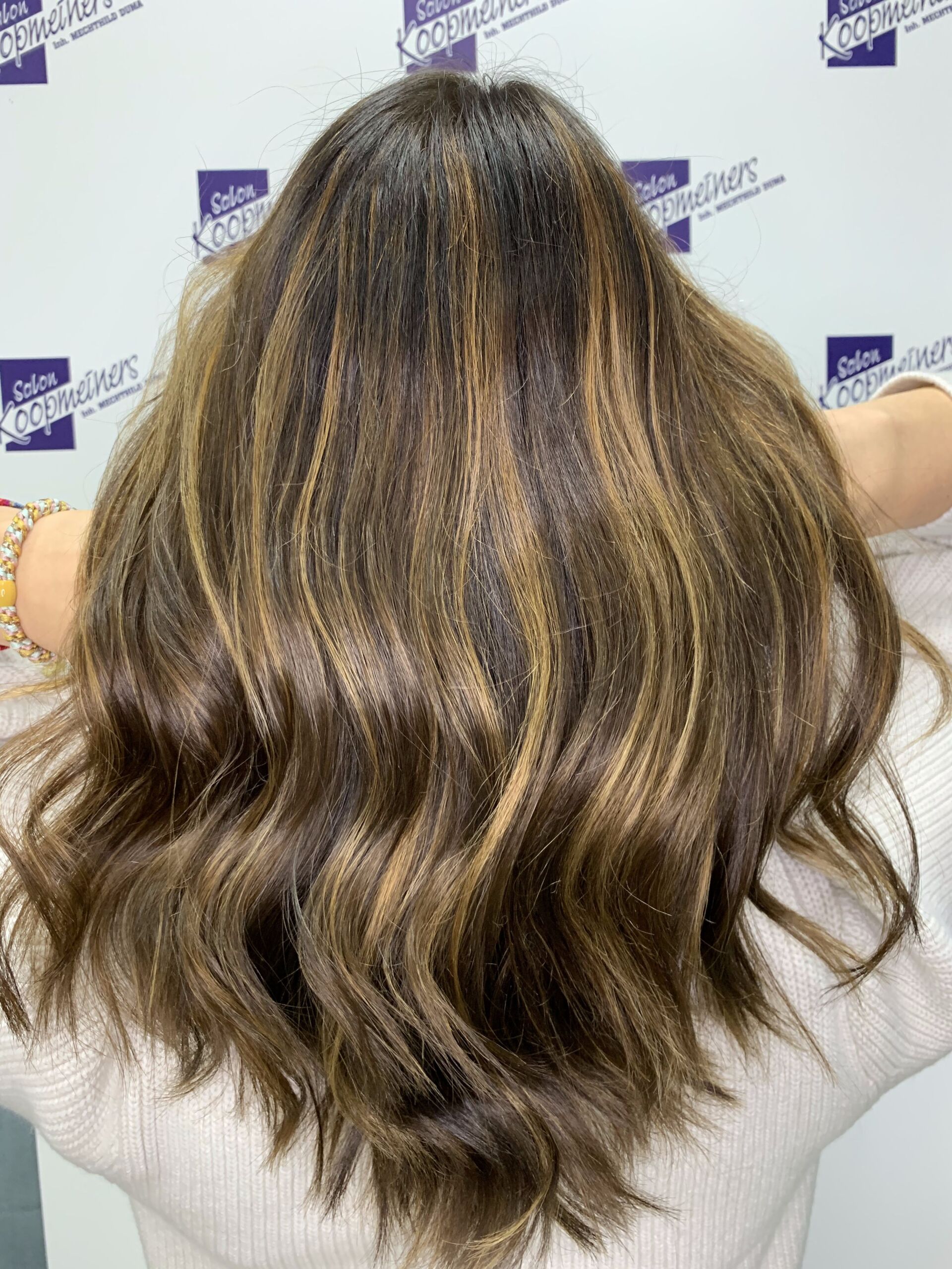 Frau mit braunem Haar und Strähnchen, mit abgewandtem Gesicht und hinter dem Kopf erhobenen Händen.