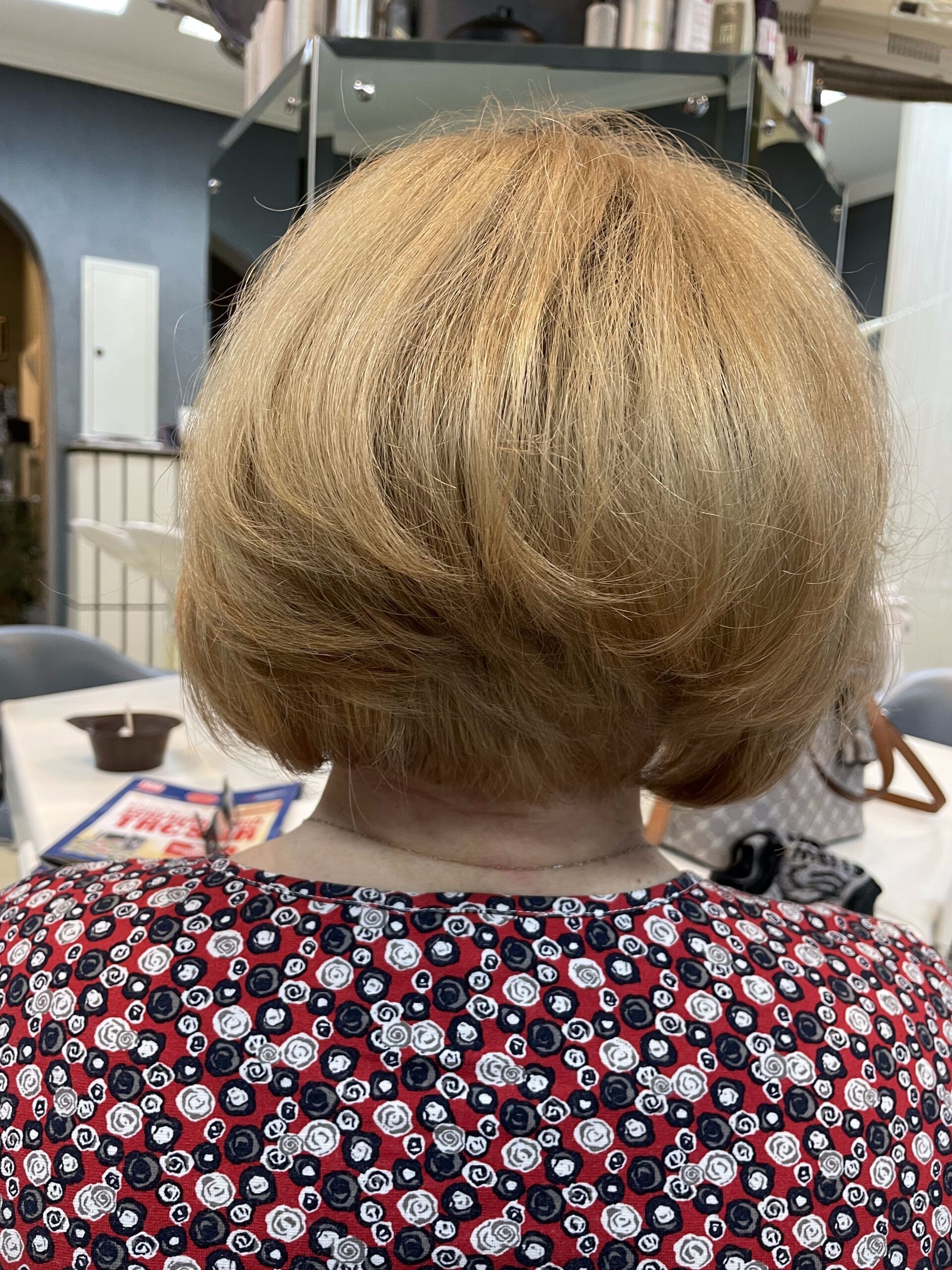 Frau mit blonder, gestufter Bobfrisur in einem Salon, trägt ein rotes Blumentop.