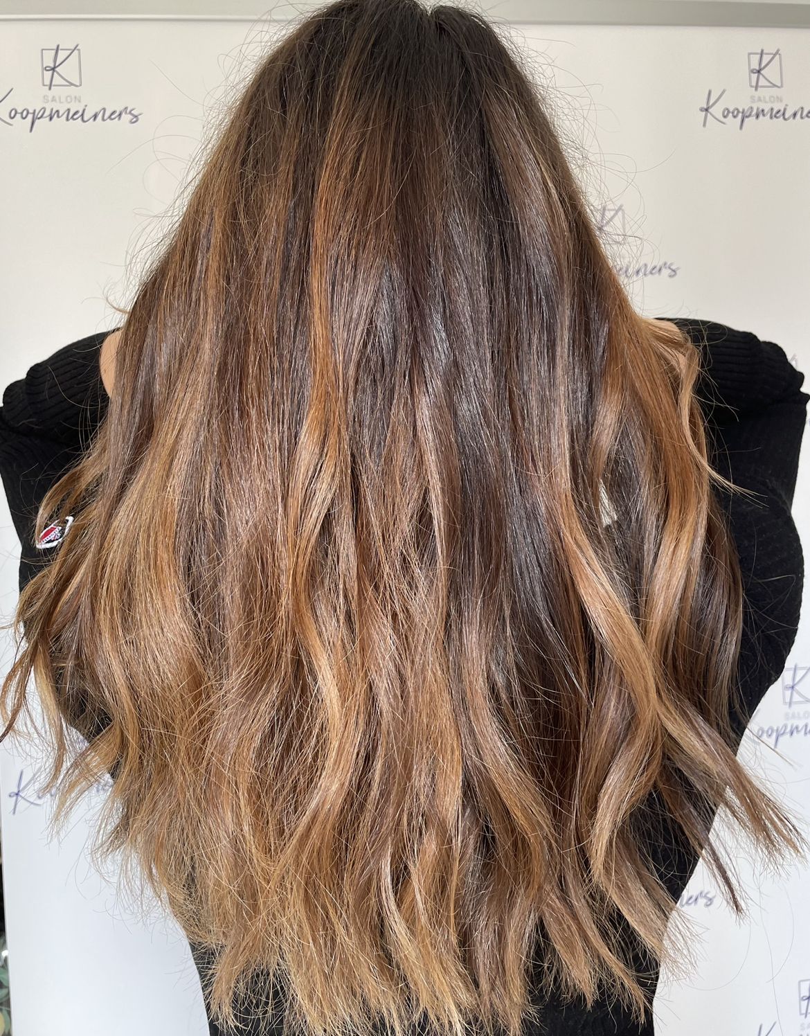 Frau mit langem, welligem, braunem und hellbraunem, gesträhntem Haar vor weißem Hintergrund.