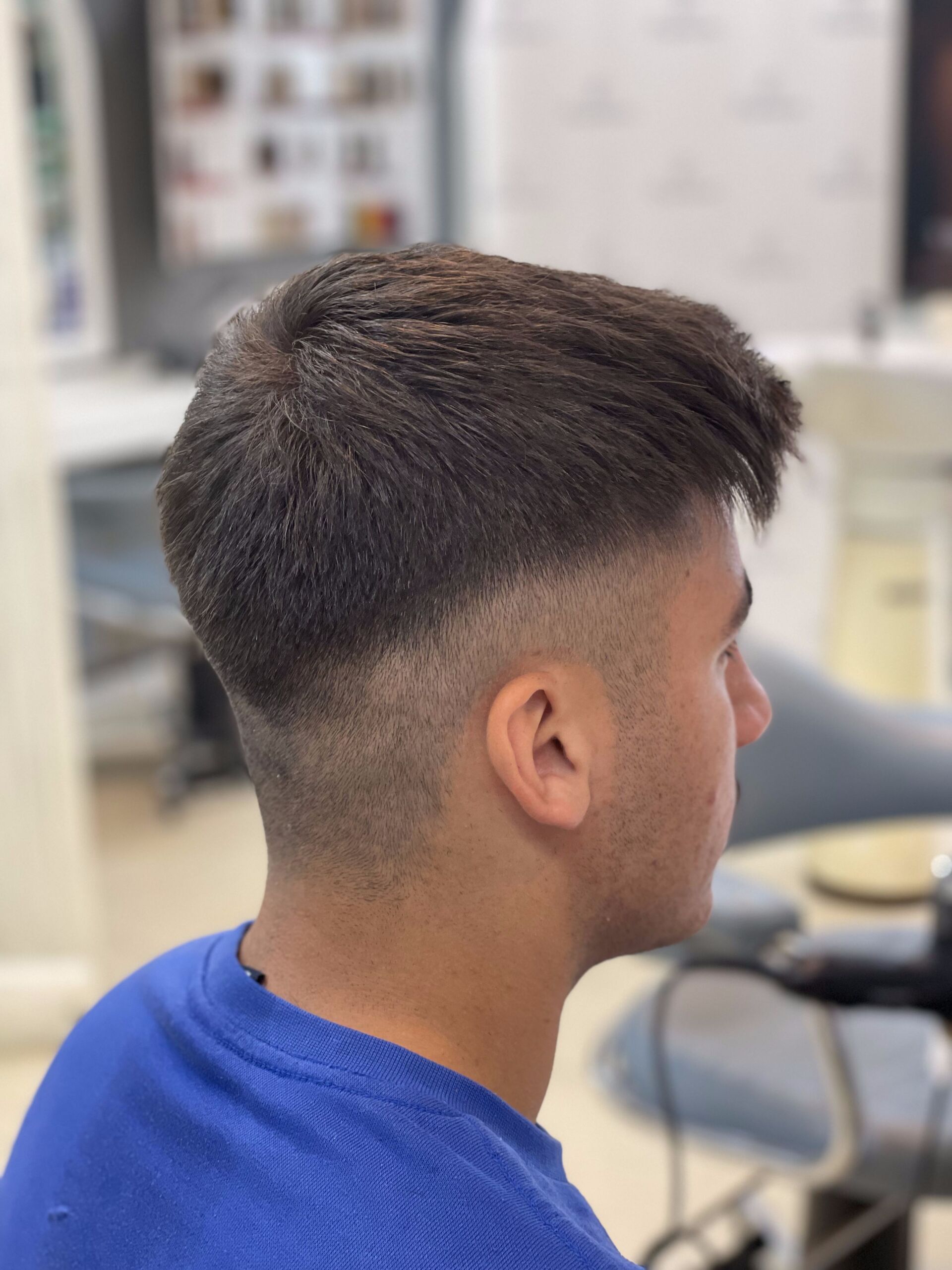 Mann mit dunklem Haar, verblasstem Haarschnitt, blauem Hemd, Seitenprofil in einem Salon.