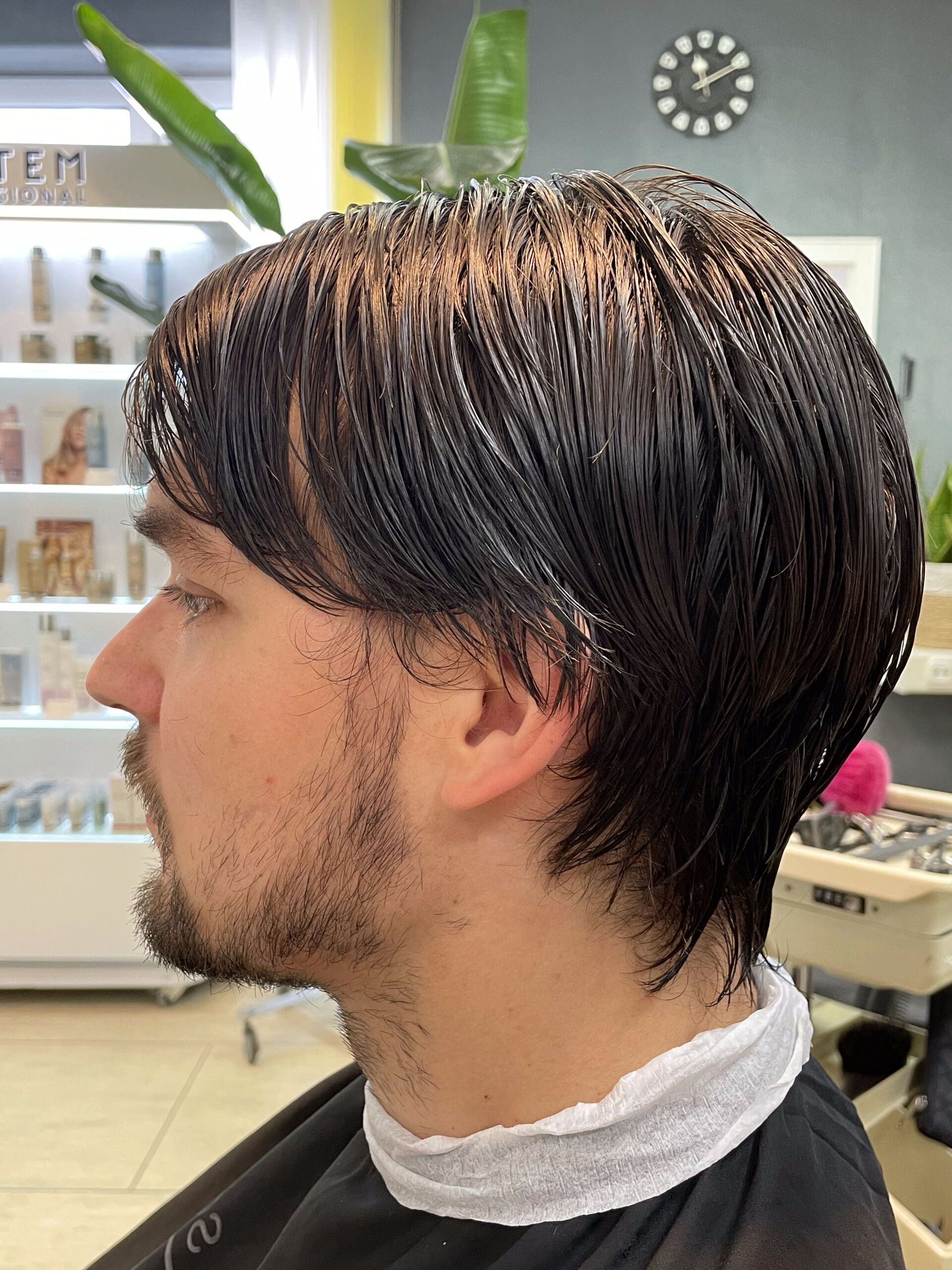 Mann mit dunklem, nassem Haar und Bartstoppeln, in einem Salon, nach links blickend.