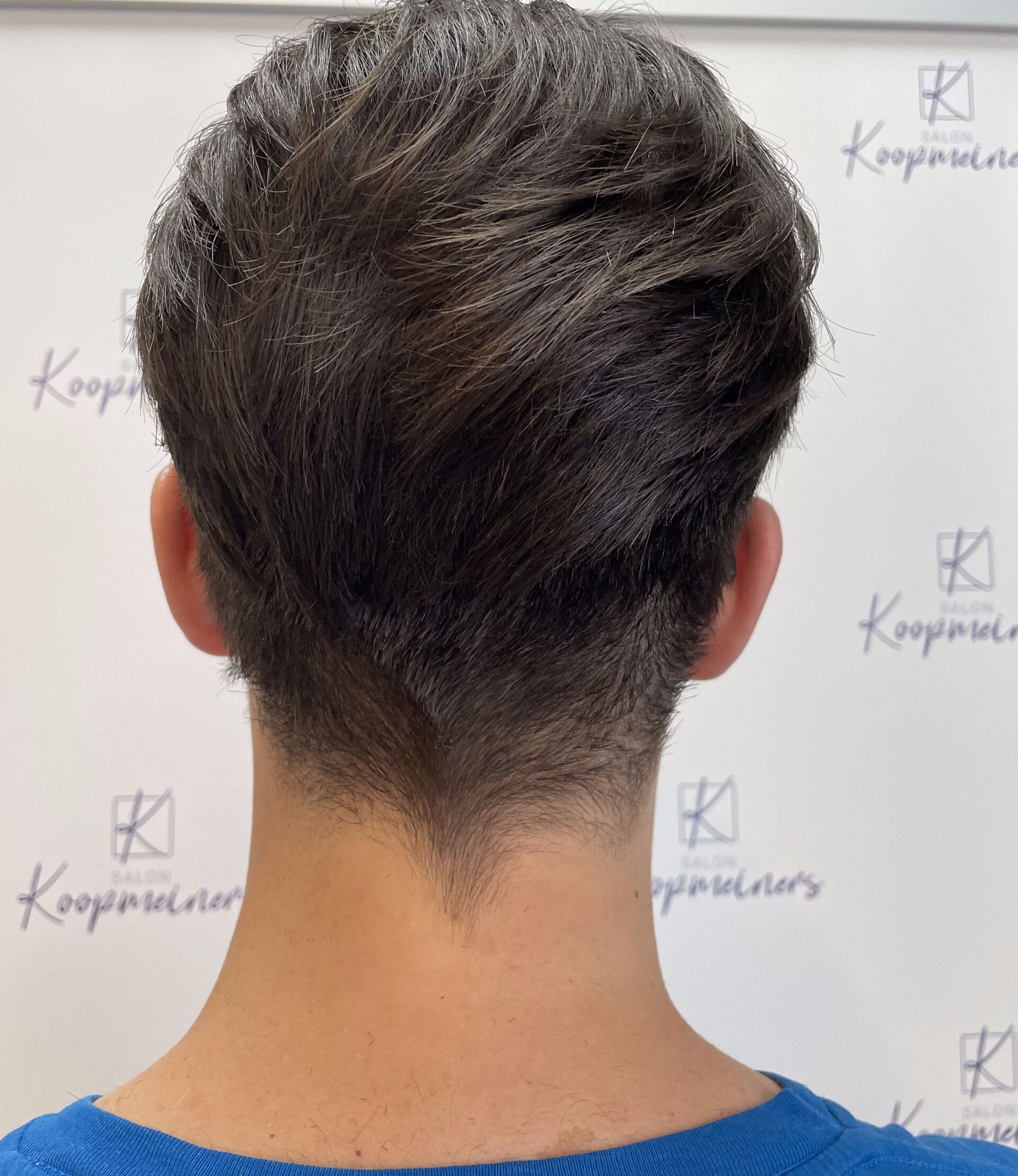 Rücken einer Person mit dunklem, strukturiertem Haar. Undercut-Stil, gepflegter Ausschnitt, vor weißem Hintergrund.