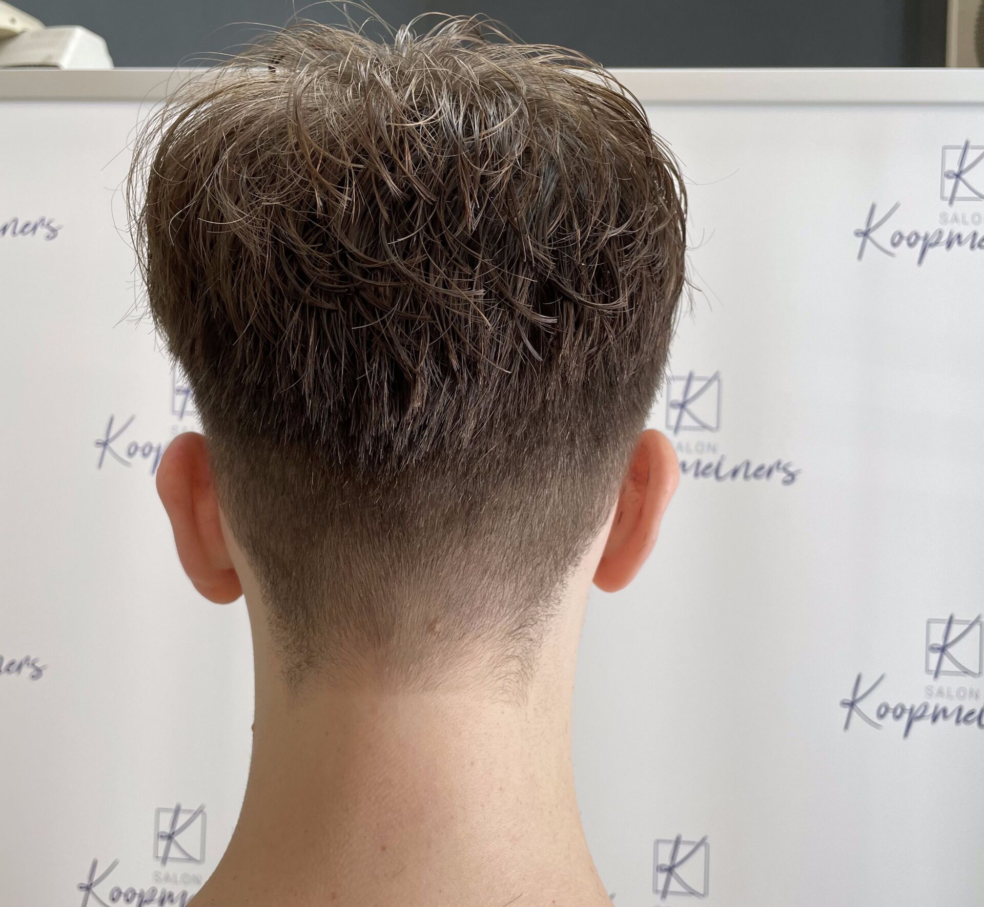 Rückansicht einer Person mit verblasstem Haarschnitt, heller Haut und weißem Hintergrund mit einem Logo.