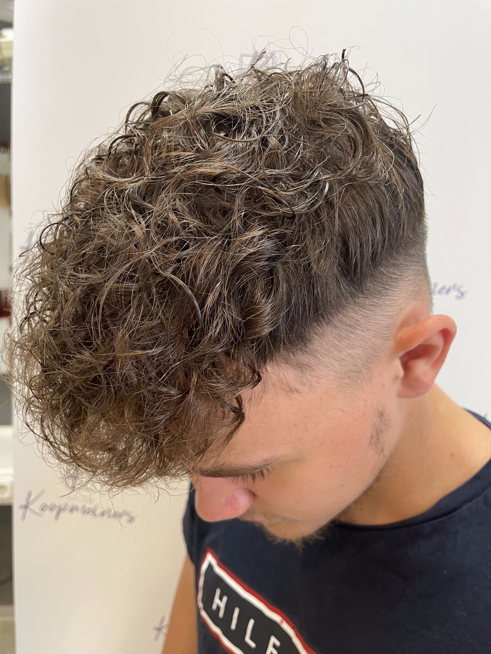 Mann mit lockigem braunem Haar und verblasstem Haarschnitt, der in einem Salon nach unten schaut.