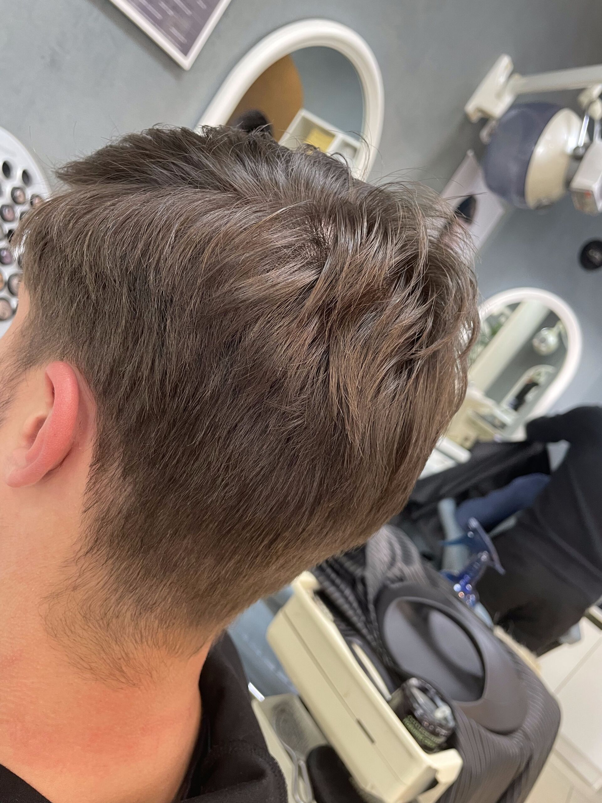 Männerhaar mit einem Fade-Effekt im Nacken und an den Seiten, von hinten in einer Salonumgebung betrachtet.