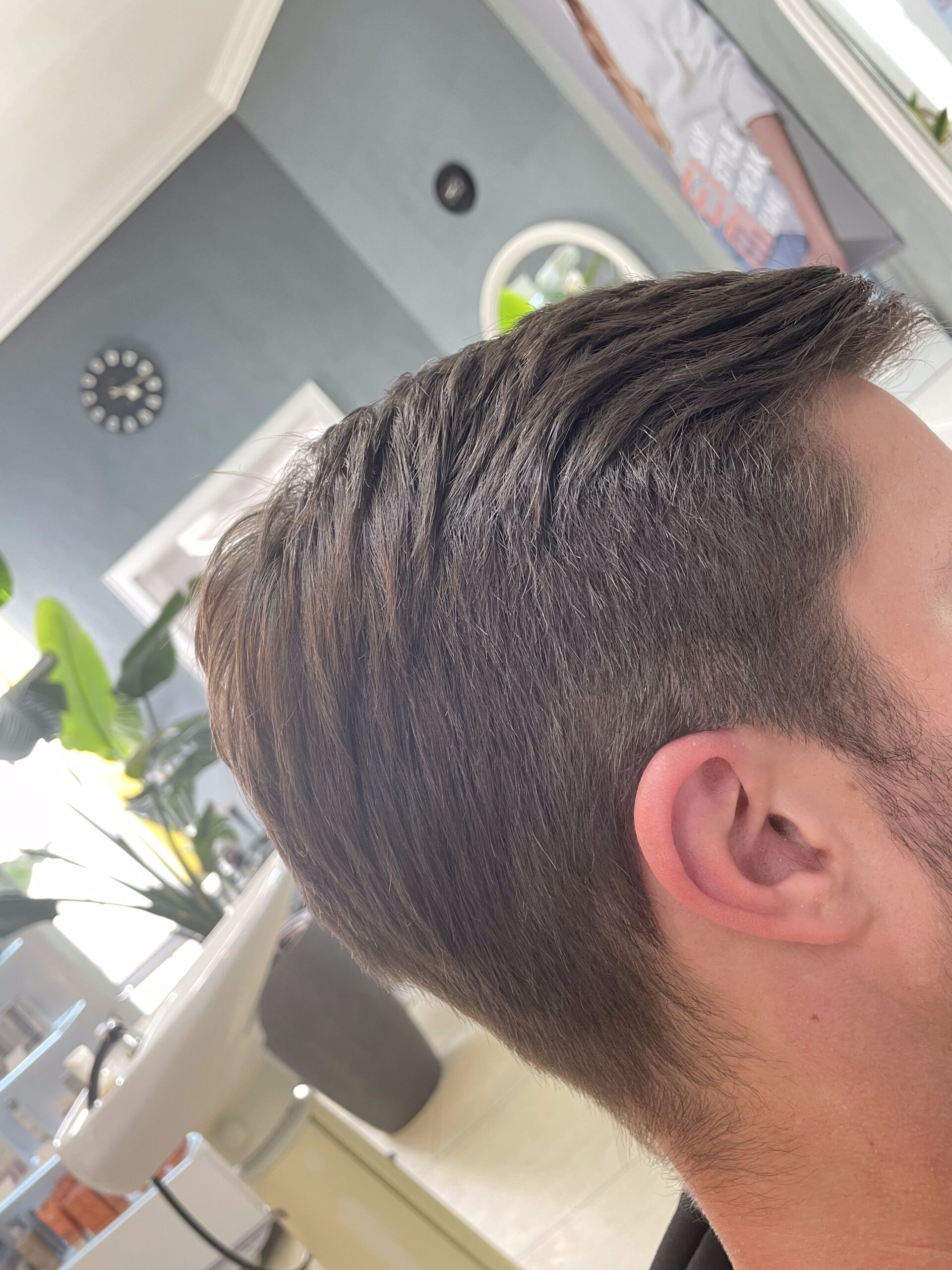 Mann mit kurzen, dunklen Haaren, nach hinten und zur Seite frisiert, in einem gut beleuchteten Raum.