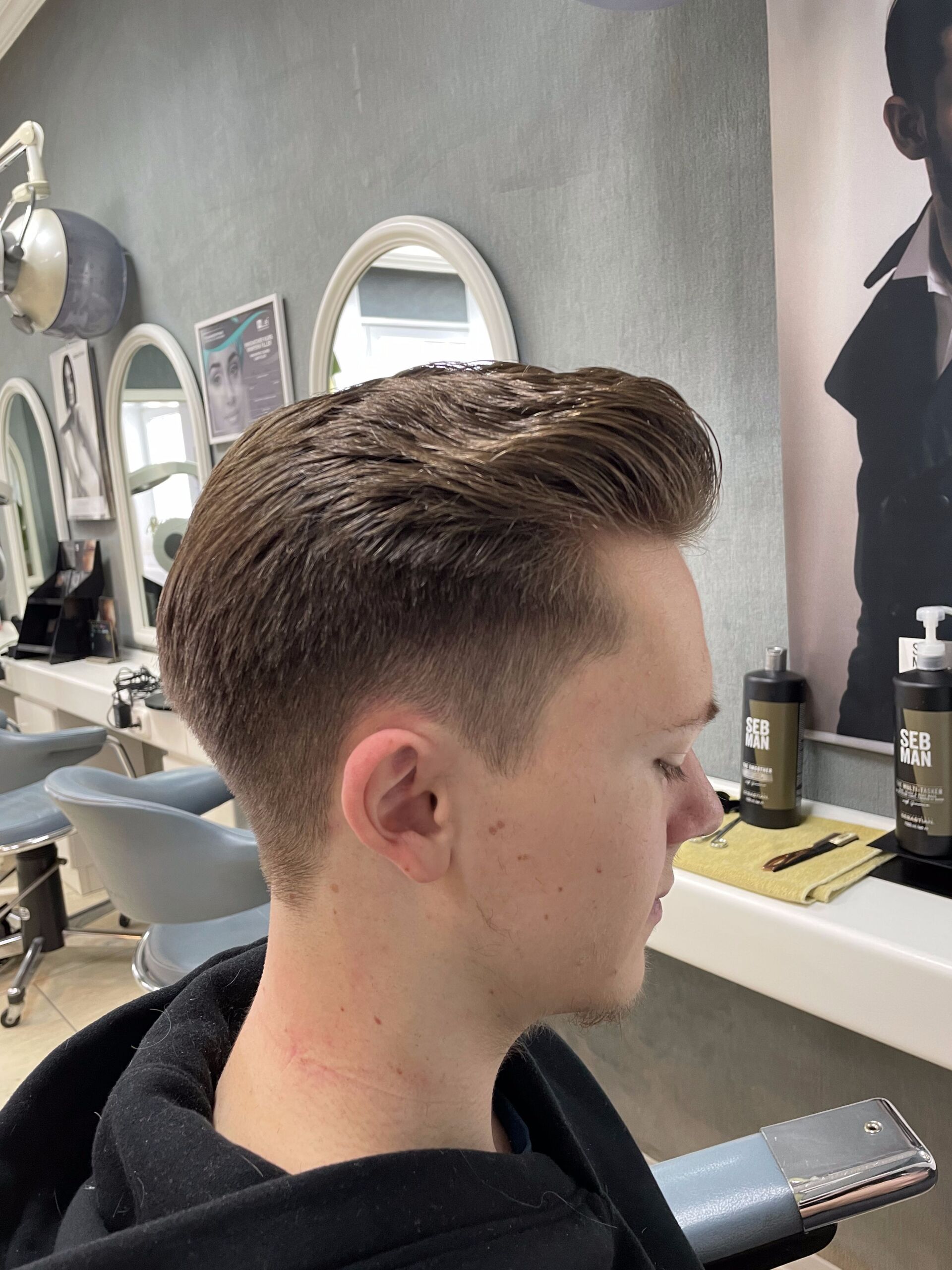 Mann mit braunem Haar, frisch geschnittenem Haar, verblassender Seite. Profilansicht in einem Salon.
