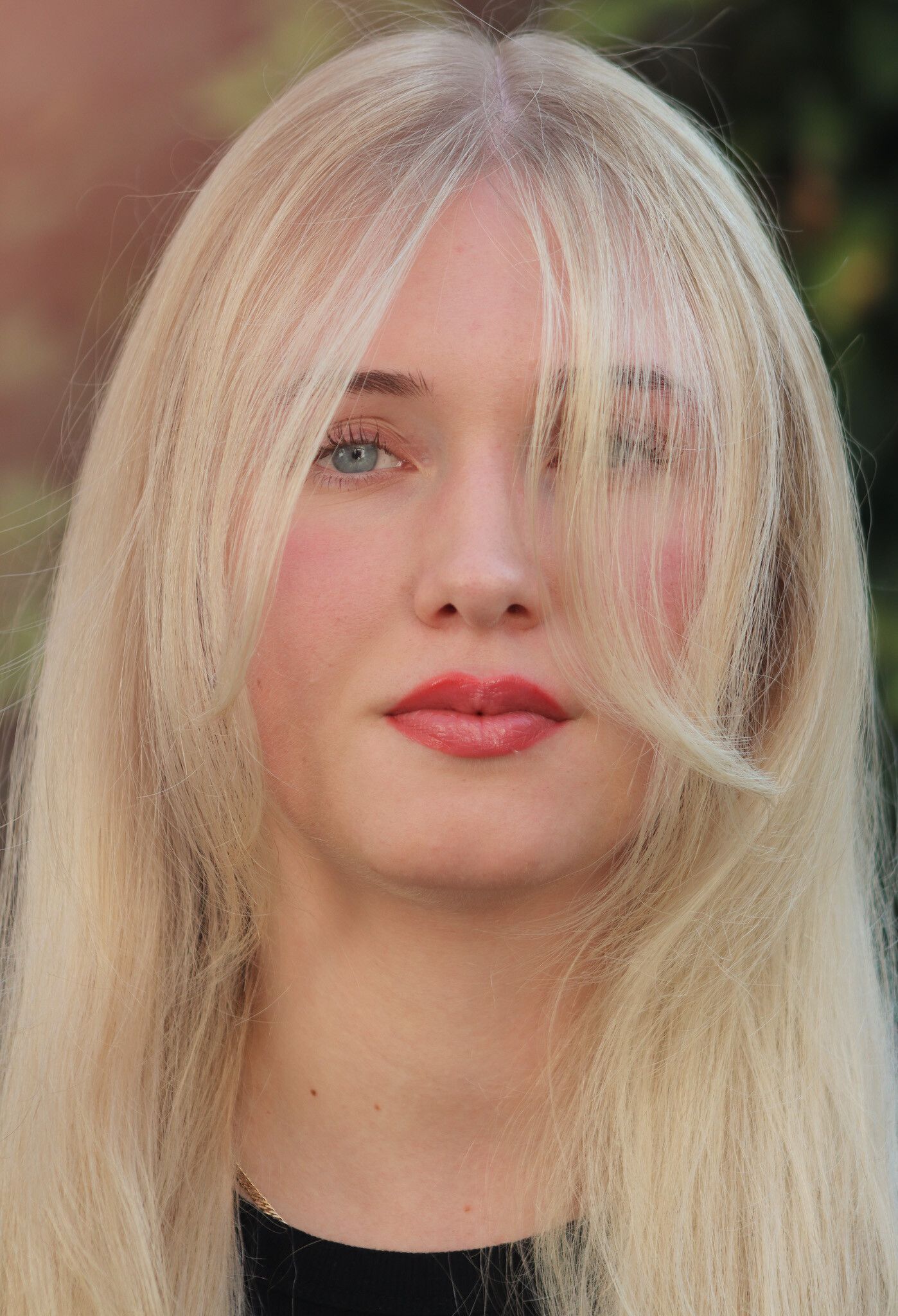 Blonde Frau mit blauen Augen, roten Lippen und langem, welligem Haar, das ihr Gesicht teilweise bedeckt.