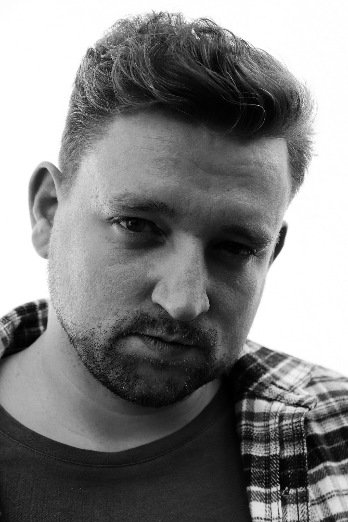 Mann im karierten Hemd, blickt mit ernstem Gesichtsausdruck nach unten, Schwarzweißfoto.