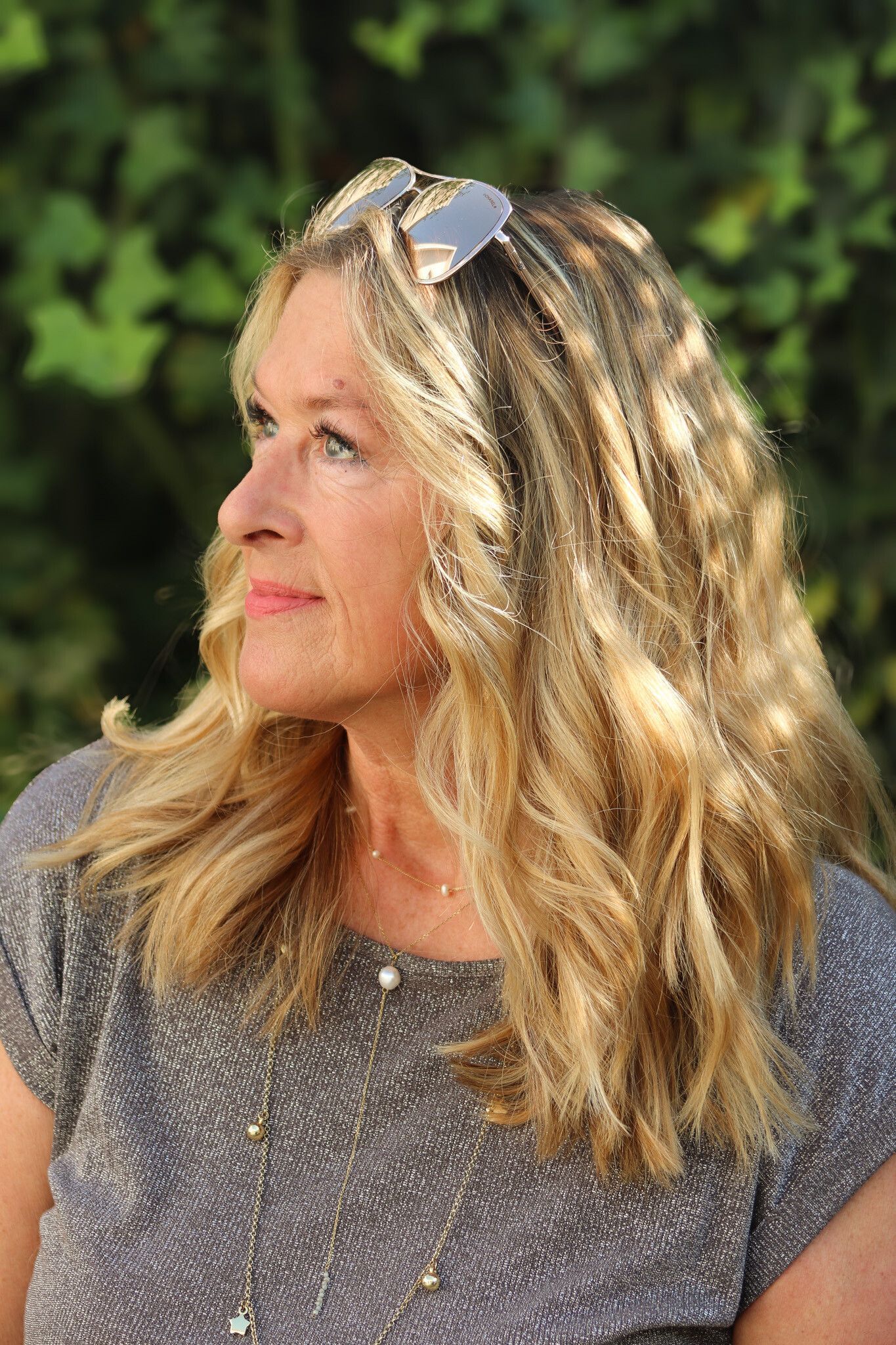 Blonde Frau mit Sonnenbrille auf dem Kopf, die mit nachdenklichem Gesichtsausdruck zur Seite schaut, nach draußen.