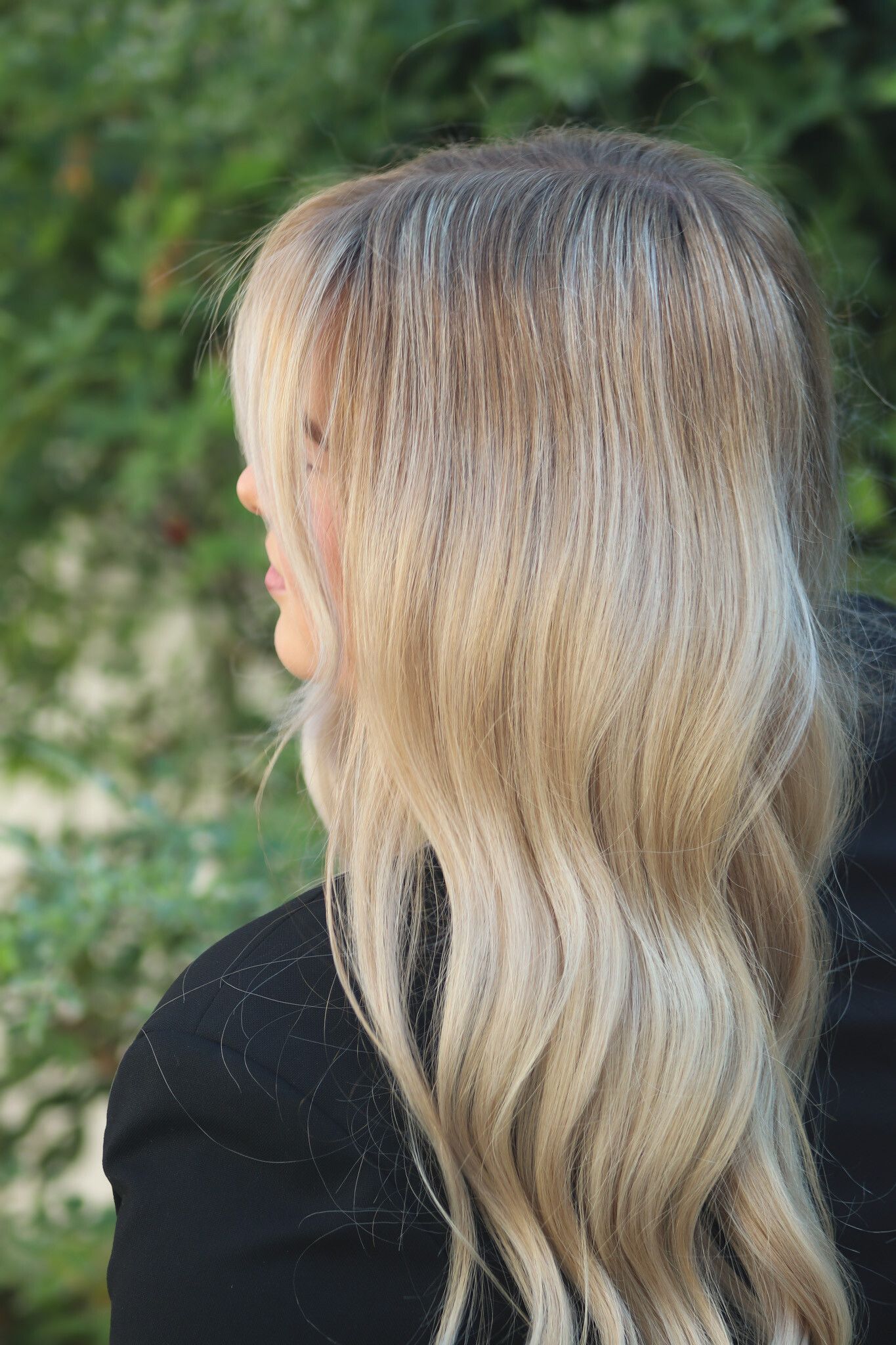 Frau mit langen, gewellten blonden Haaren und einer schwarzen Jacke, Seitenprofil.