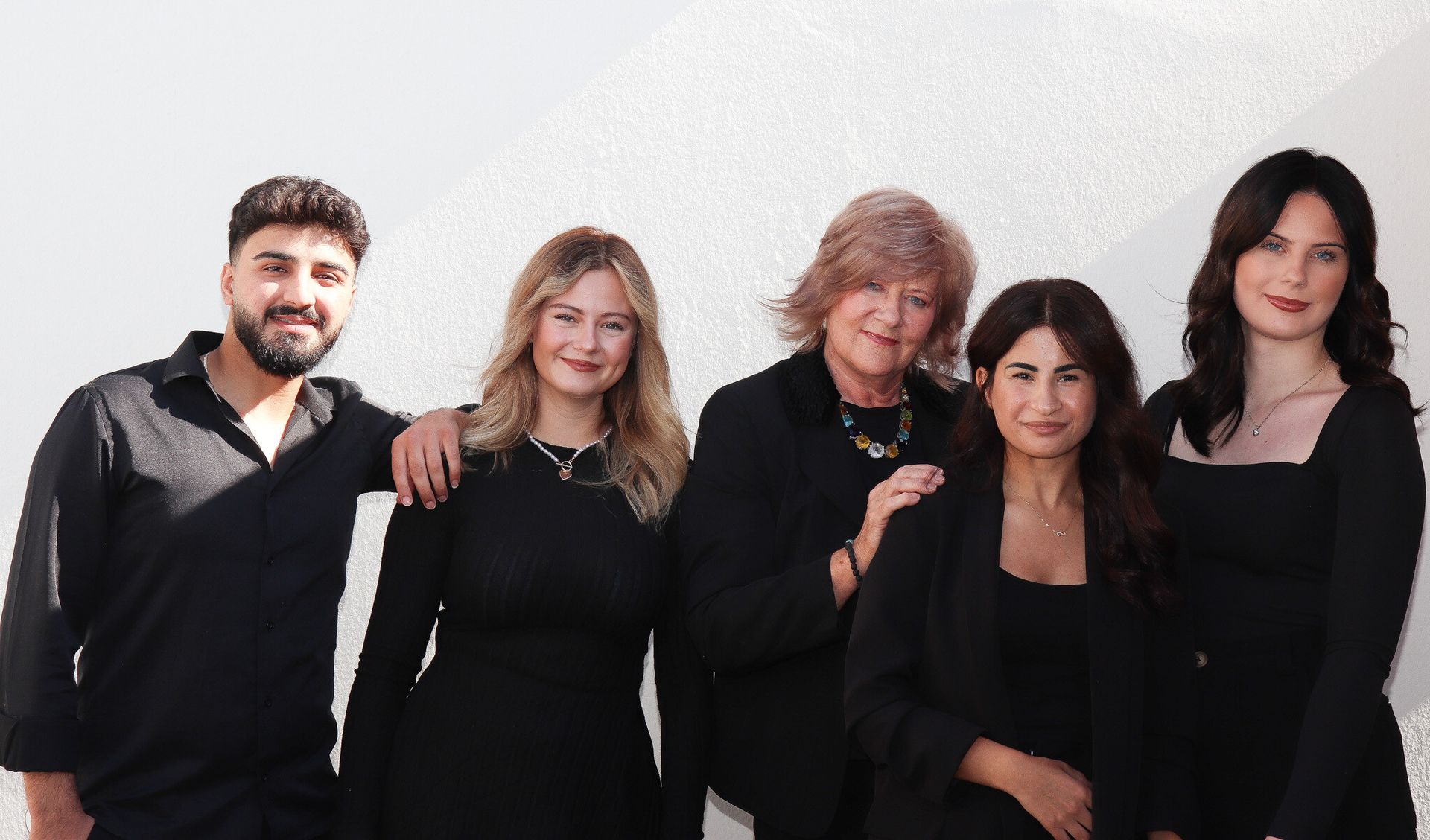 Fünf Personen in dunkler Kleidung posieren vor einem weißen Hintergrund.