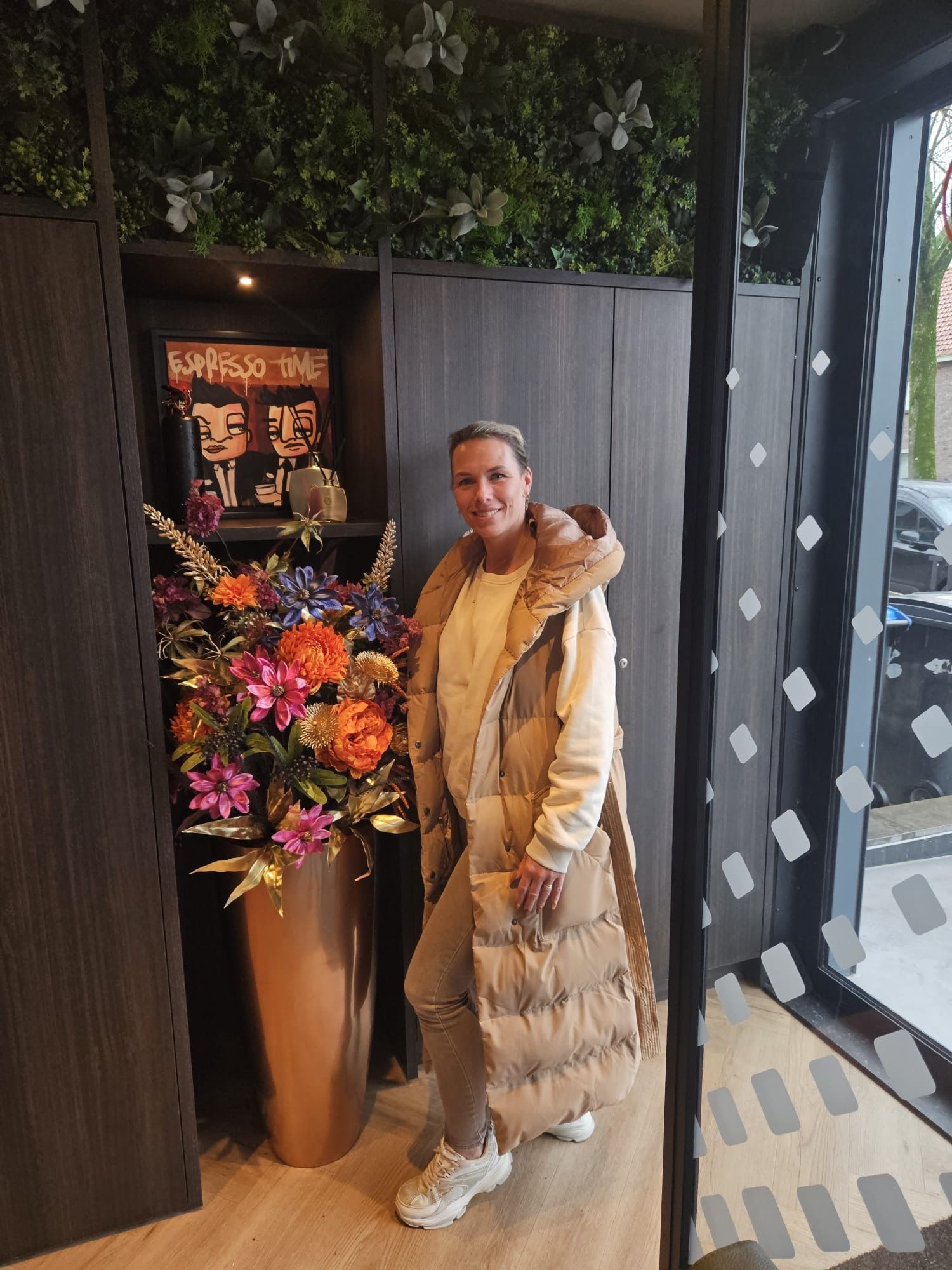 Een vrouw staat voor een vaas met bloemen in een kamer.