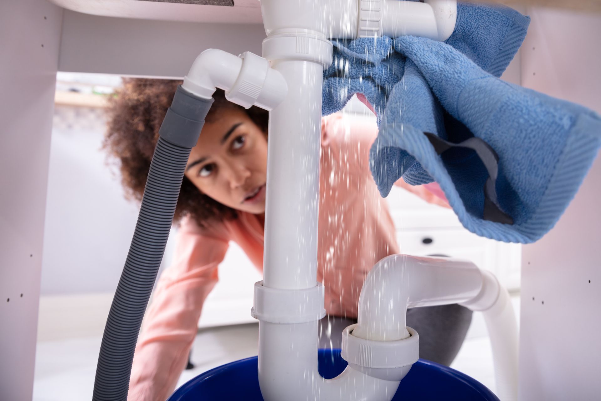 Close-up of a young woman using soft blue napkin under leakage of white sink pipe.
