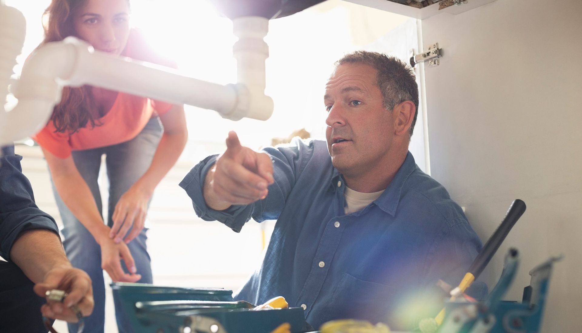 Plumbers working on pipes under sink