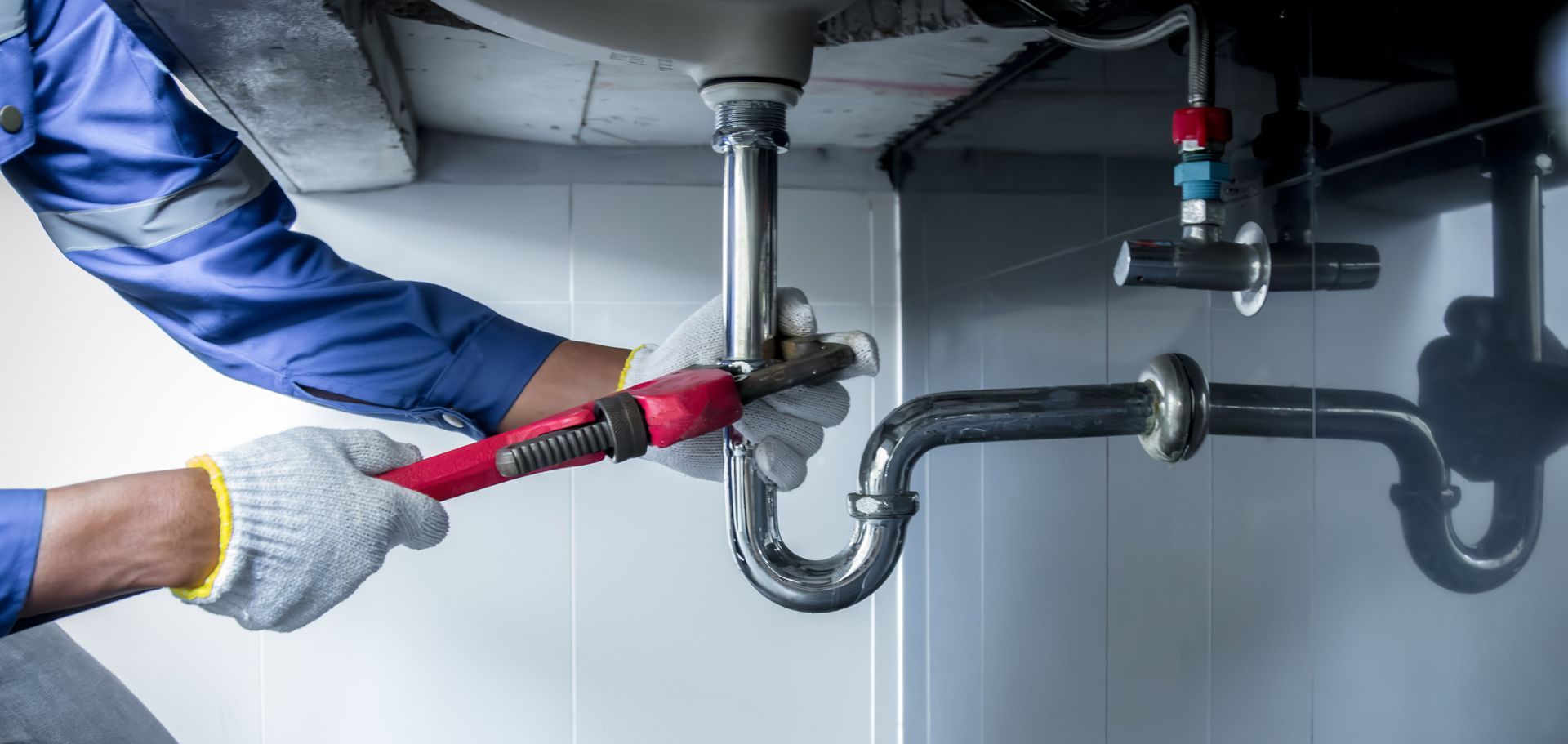 Plumber using a wrench to repair piping beneath a kitchen sink. Plumber using a wrench to repair piping beneath a kitchen sink.