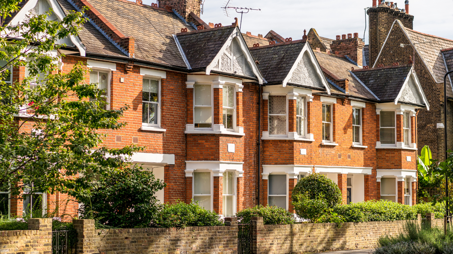 A row of brick houses on a sunny day with trees in front of them.