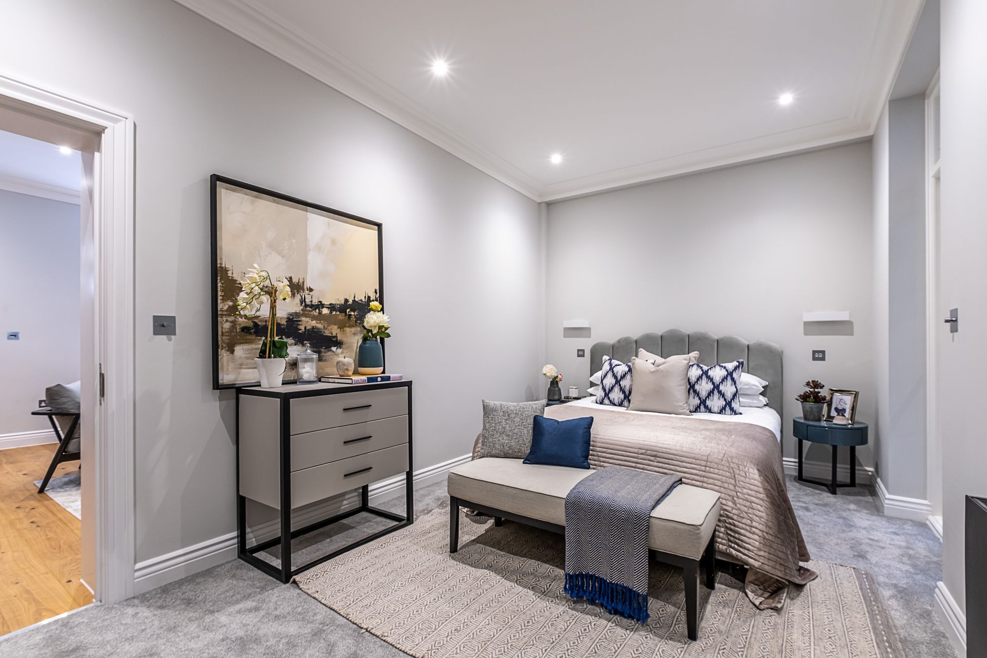 A bedroom with a large bed , dresser , bench and painting on the wall.