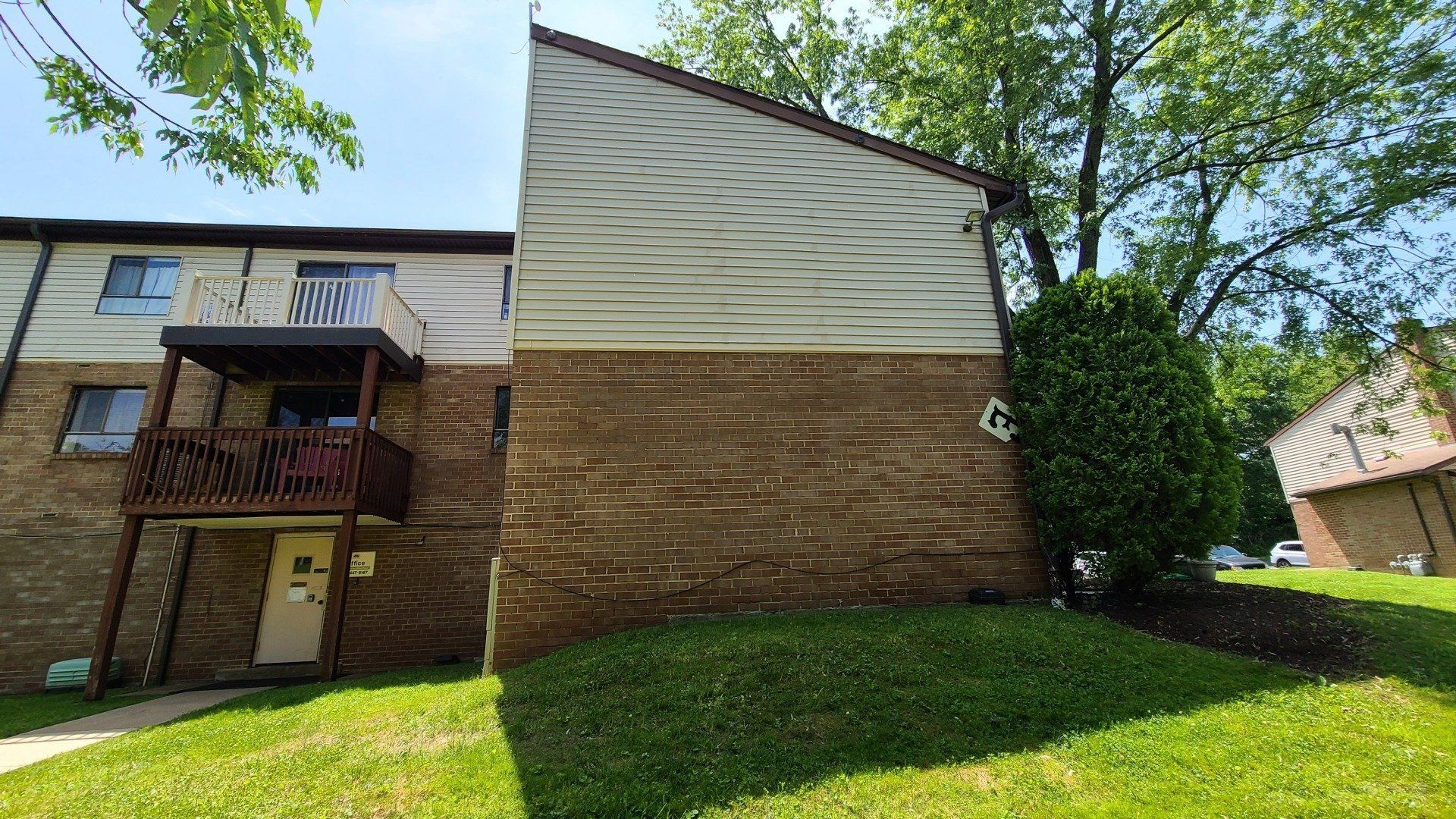 Apartment building exterior, beige siding, brown brick base, green lawn, tree, sunny day.