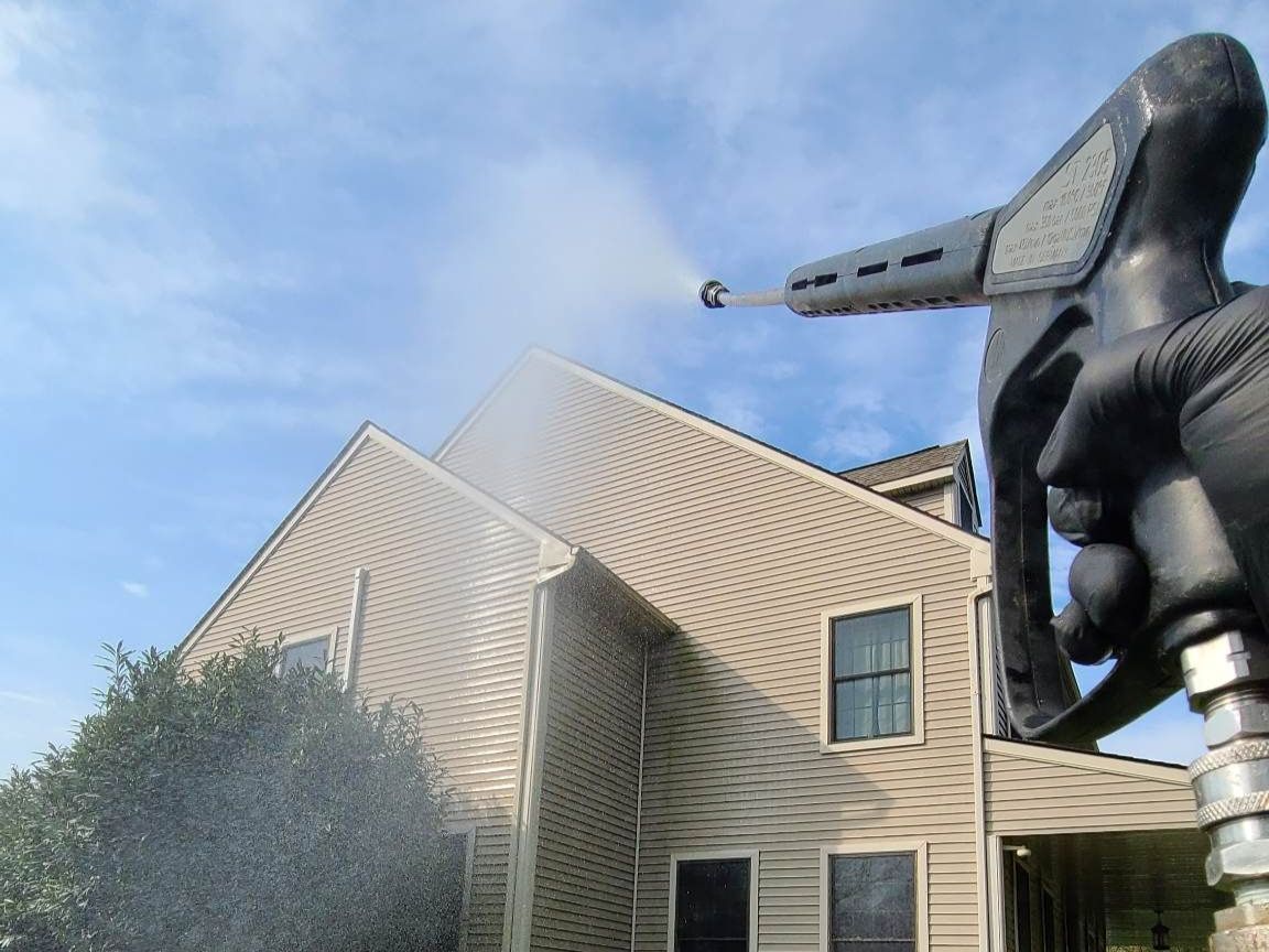 A person power washing a house with a pressure washer; blue sky background.