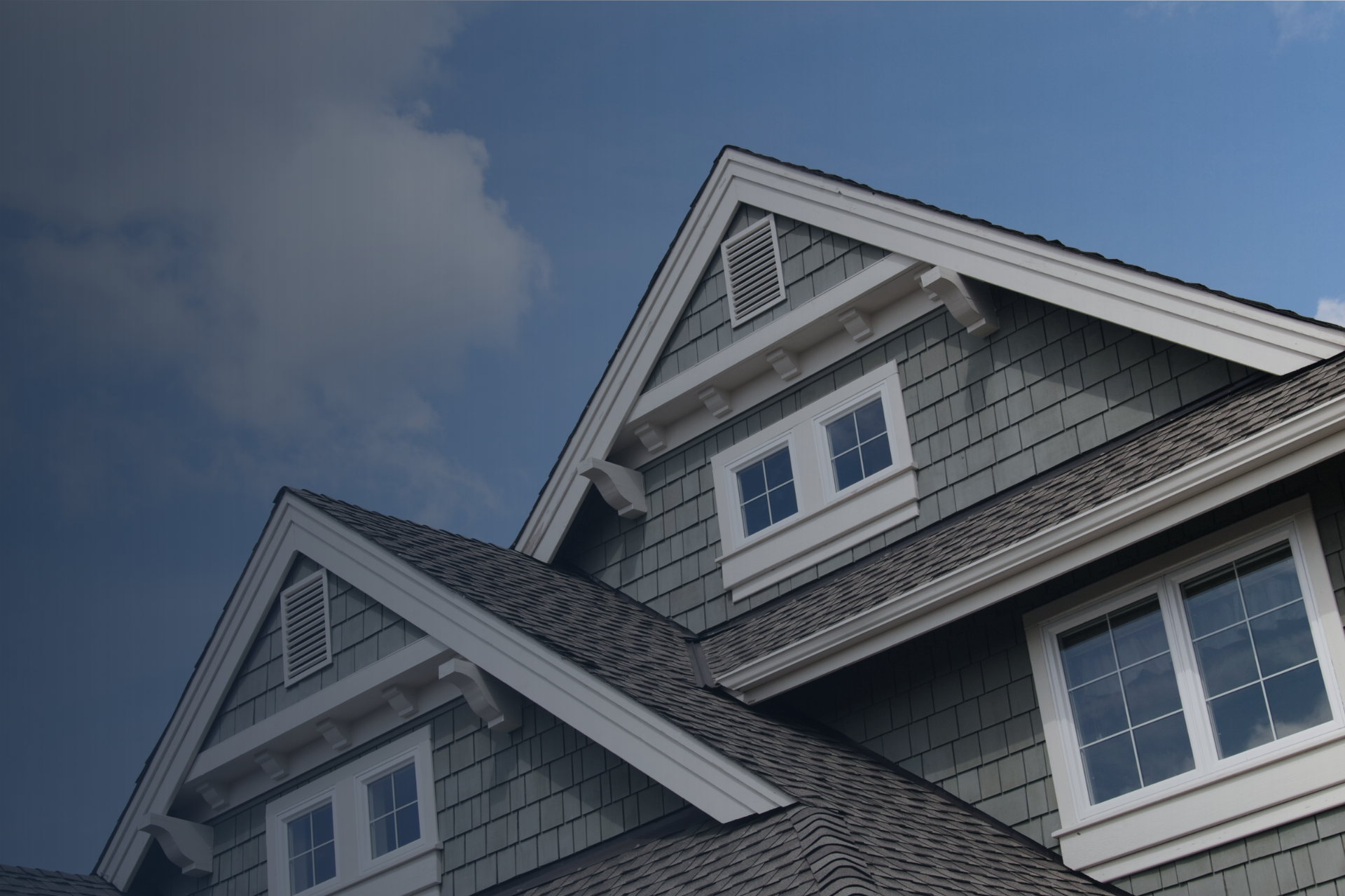 Blue house exterior with gray roof and white trim against a partly cloudy sky.