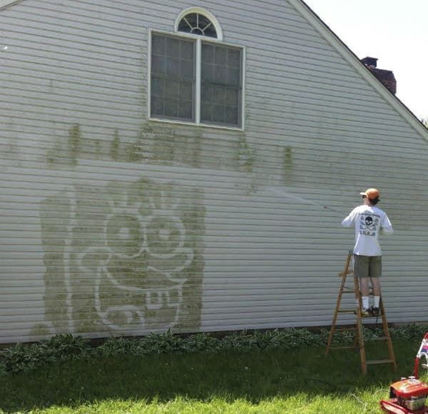 Person power washing side of house, revealing a cartoon image of Spongebob Squarepants.