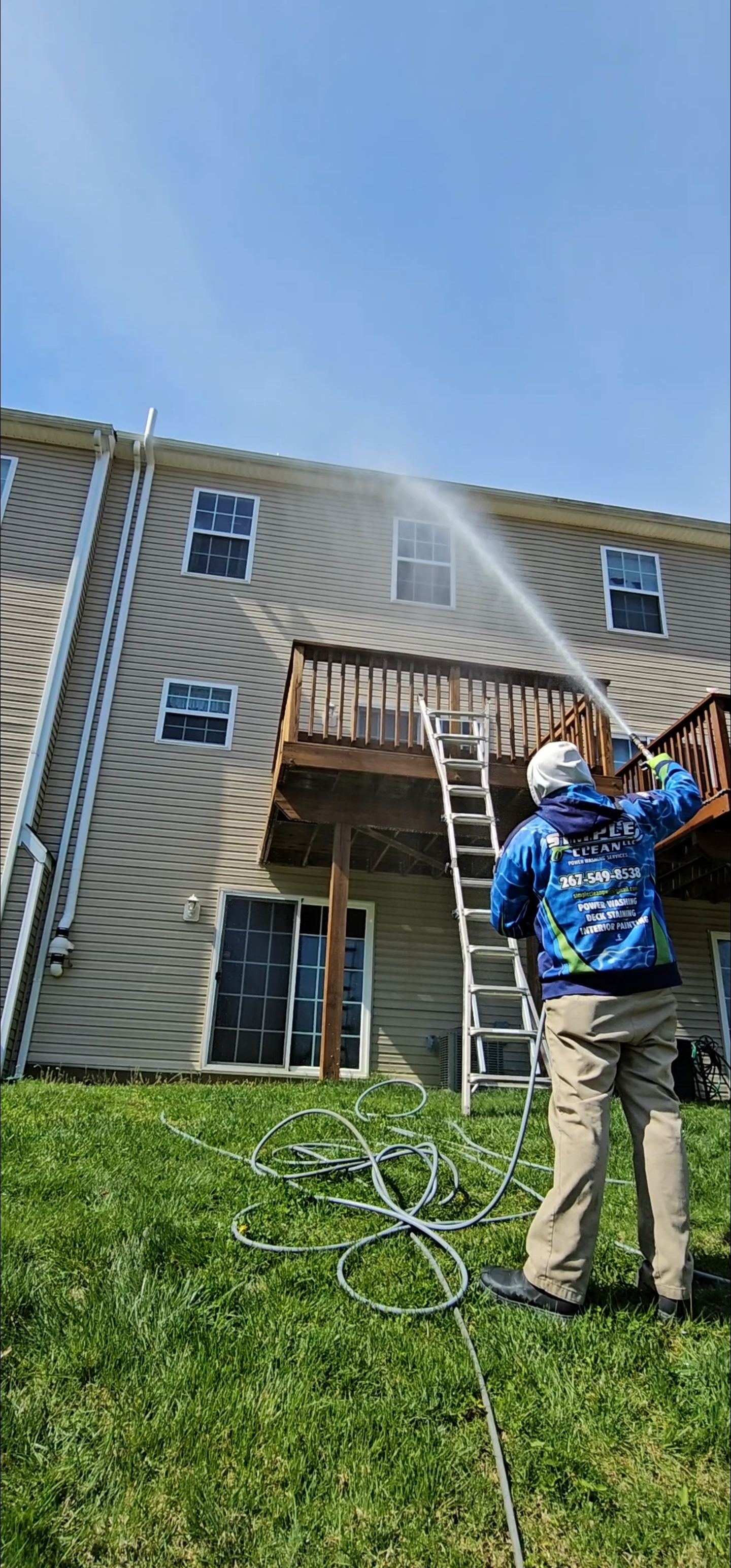 Person power washing a two-story building with a wooden deck. The person is using a hose with high-pressure water.