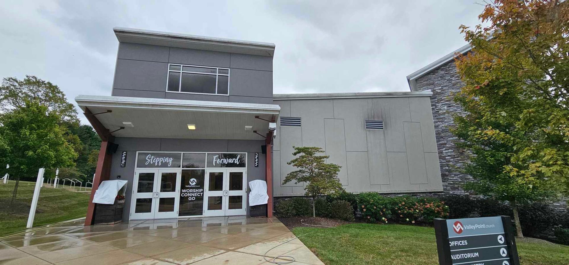 A modern building with a grey exterior and glass doors. A sign reads 