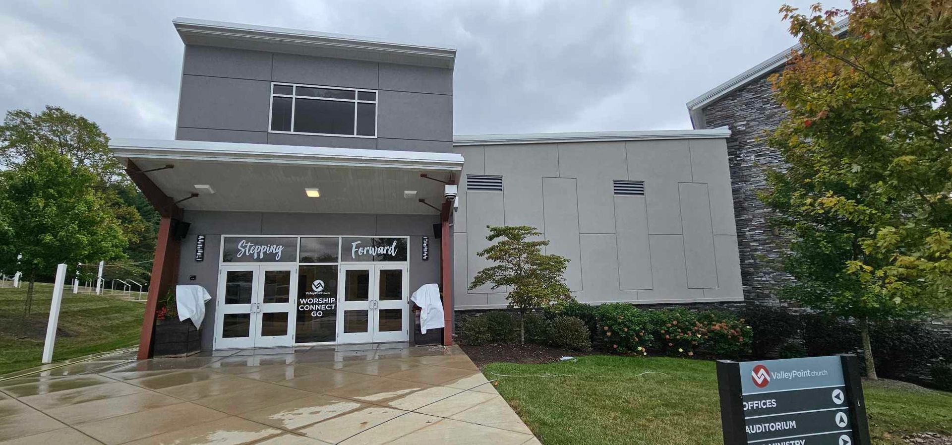 Modern building entrance with large windows and sign, under a cloudy sky.