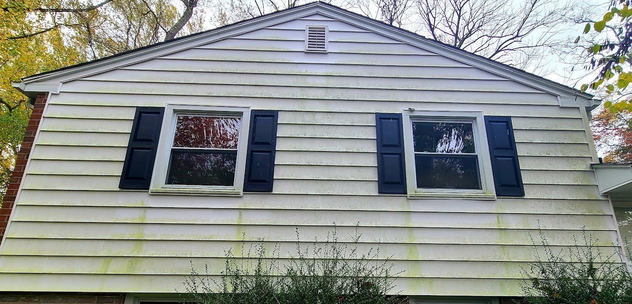 Exterior view of a weathered white house with black shutters on the windows.