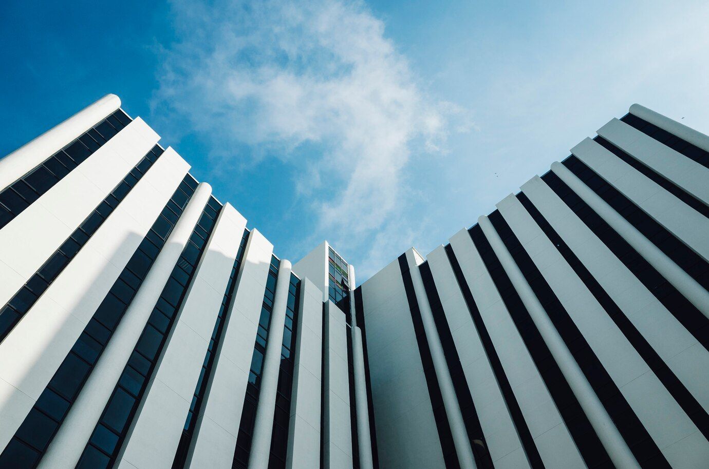 White and black striped modern building against a blue sky with clouds.